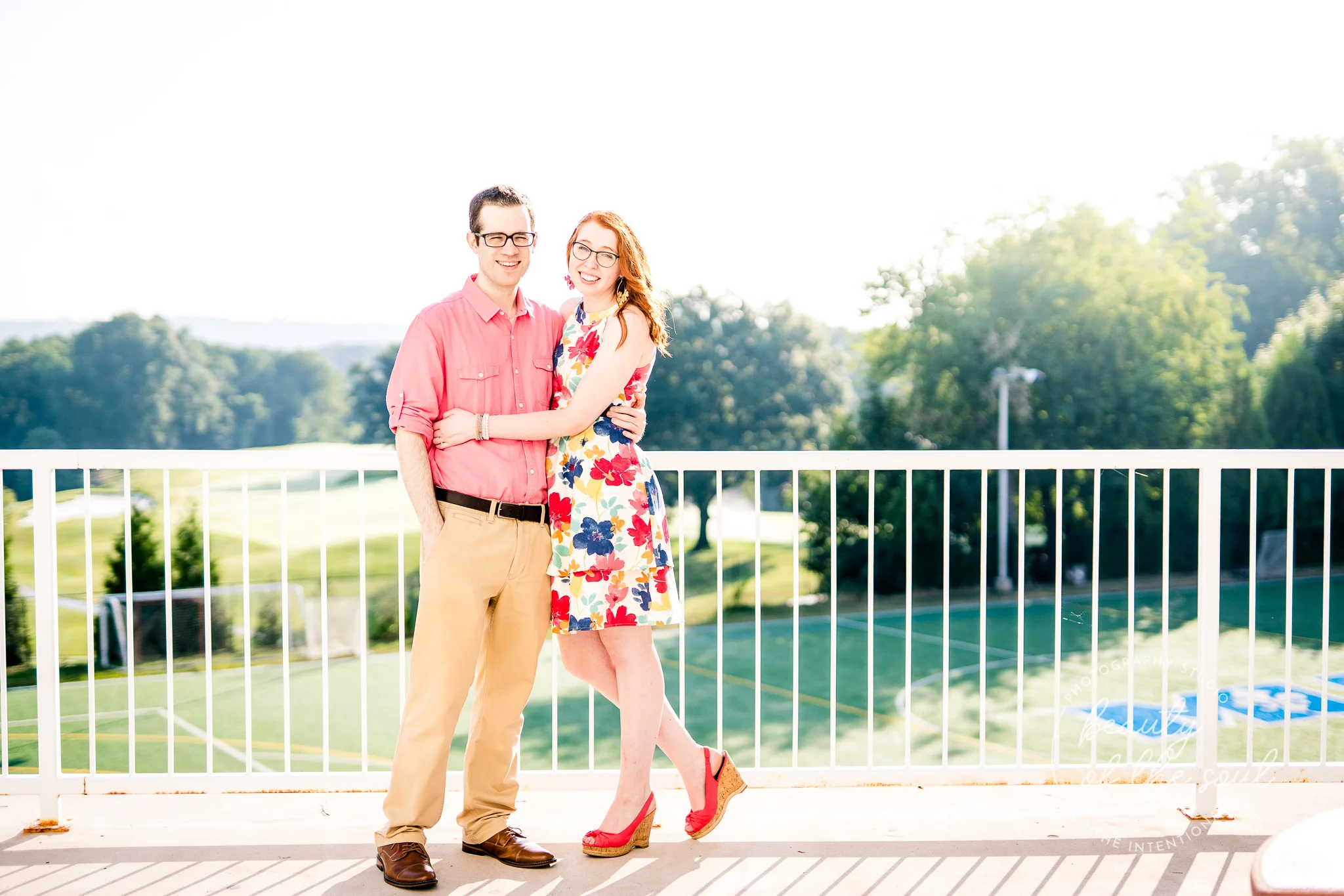 An engaged couple stand and pose together on the balcony of Rowley Hall at Marymount University during their summer sunrise engagement session in Arlington, Northern Virginia