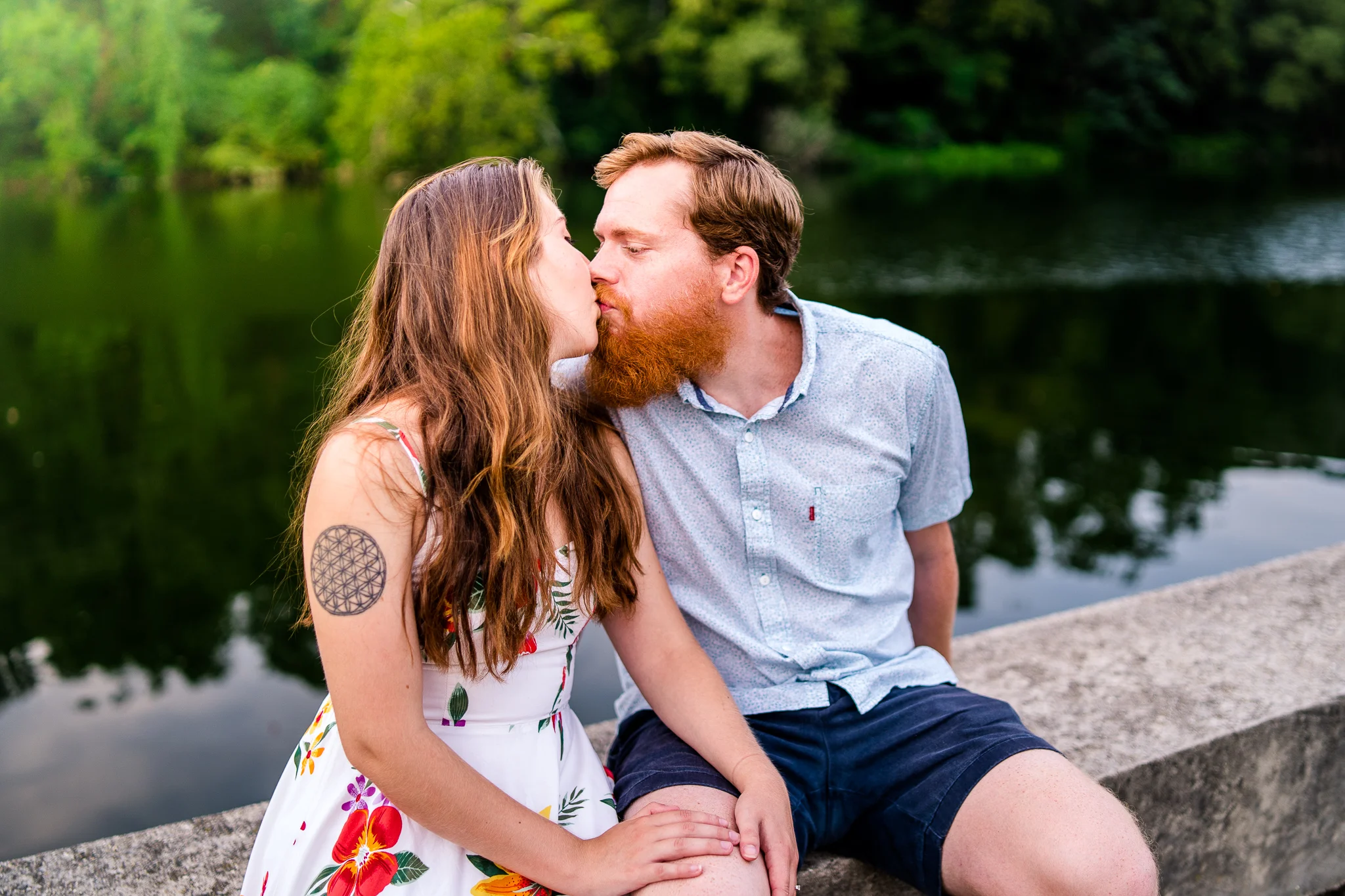 An engaged couple shares a kiss by the water during their summer sunset engagement session in Historic Occoquan, Northern Virginia