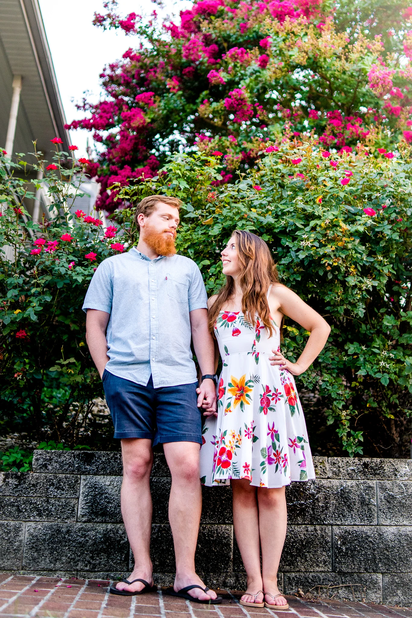 An engaged couple stands together in front of a flower garden during their summer sunset engagement session in Historic Occoquan, Northern Virginia