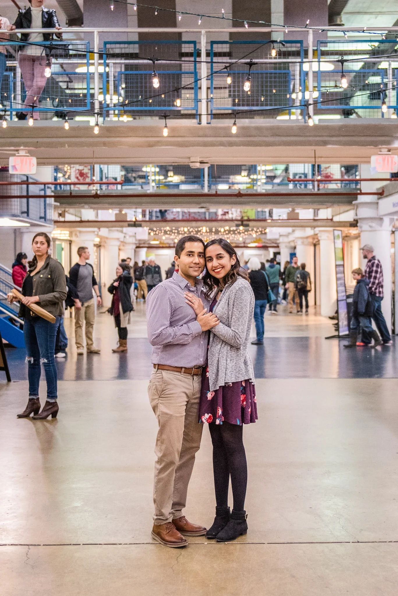 An engaged couple stands together inside the busy Torpedo Factory Art Center during their engagement session in Old Town Alexandria