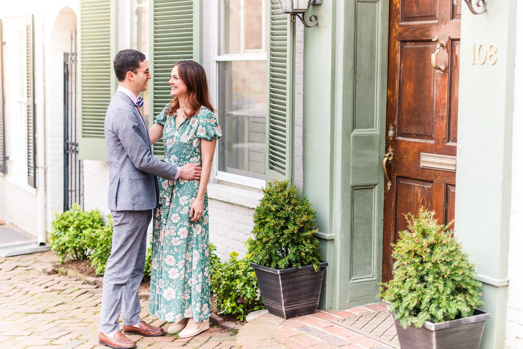 An engaged couple stand together on the sidewalk outside a historic building during their engagement session in Old Town Alexandria