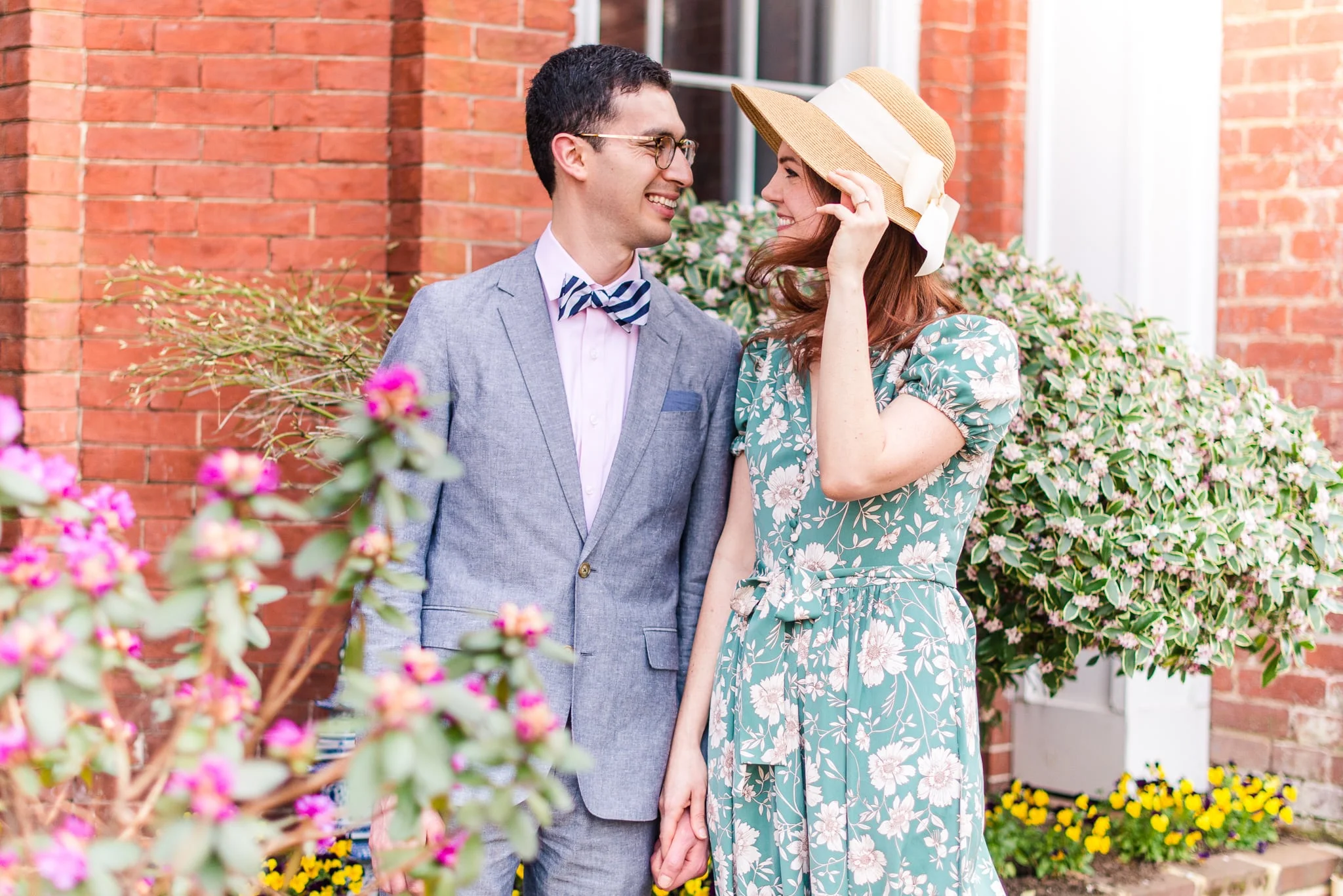 An engaged couple stands together as a breeze blows through the spring flowers around them during their engagement session in Old Town Alexandria
