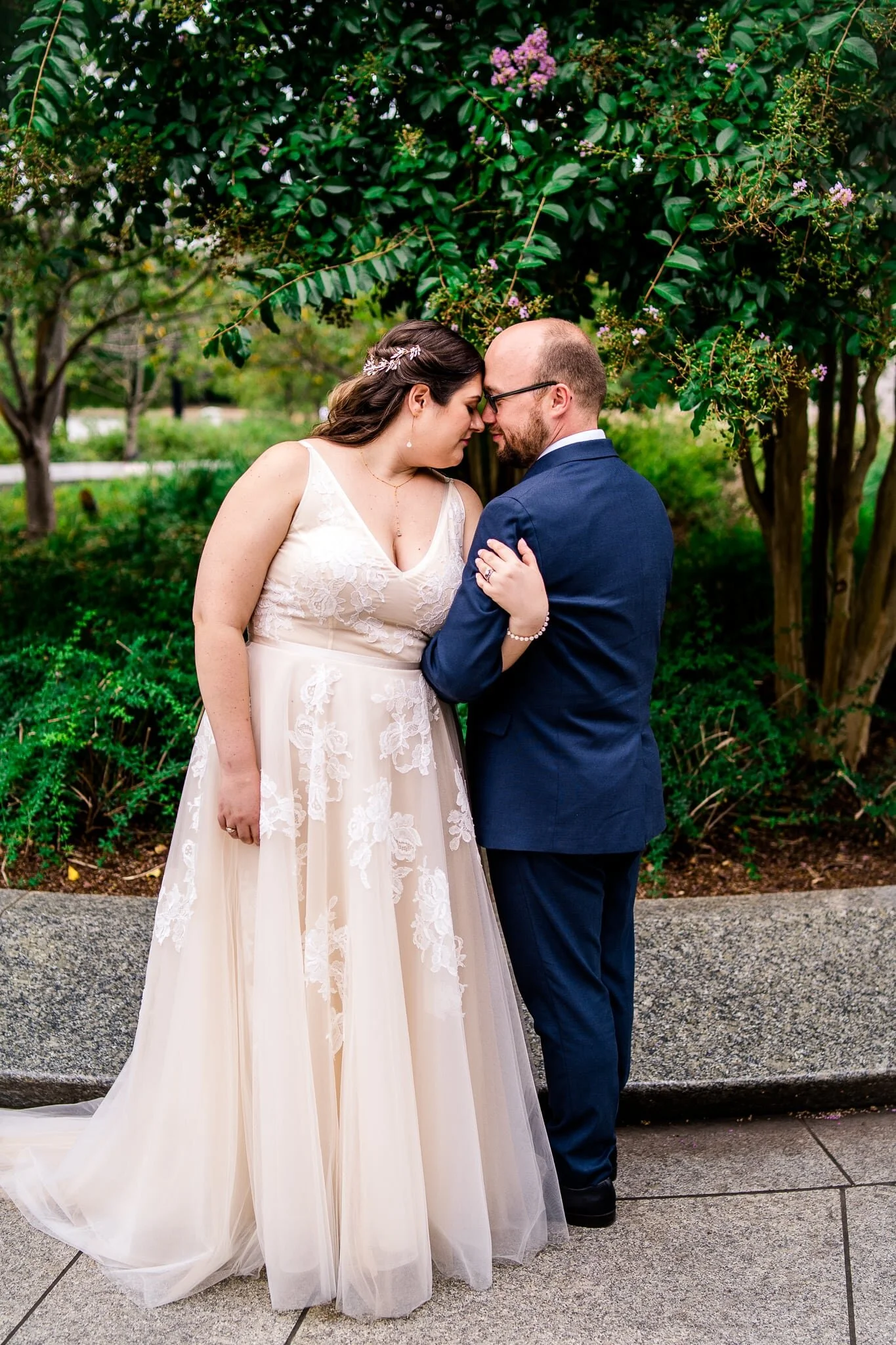 A bride and groom stand together arm in arm with foreheads together on their wedding day at the Tidal Basin by the MLK Memorial in Washington, DC
