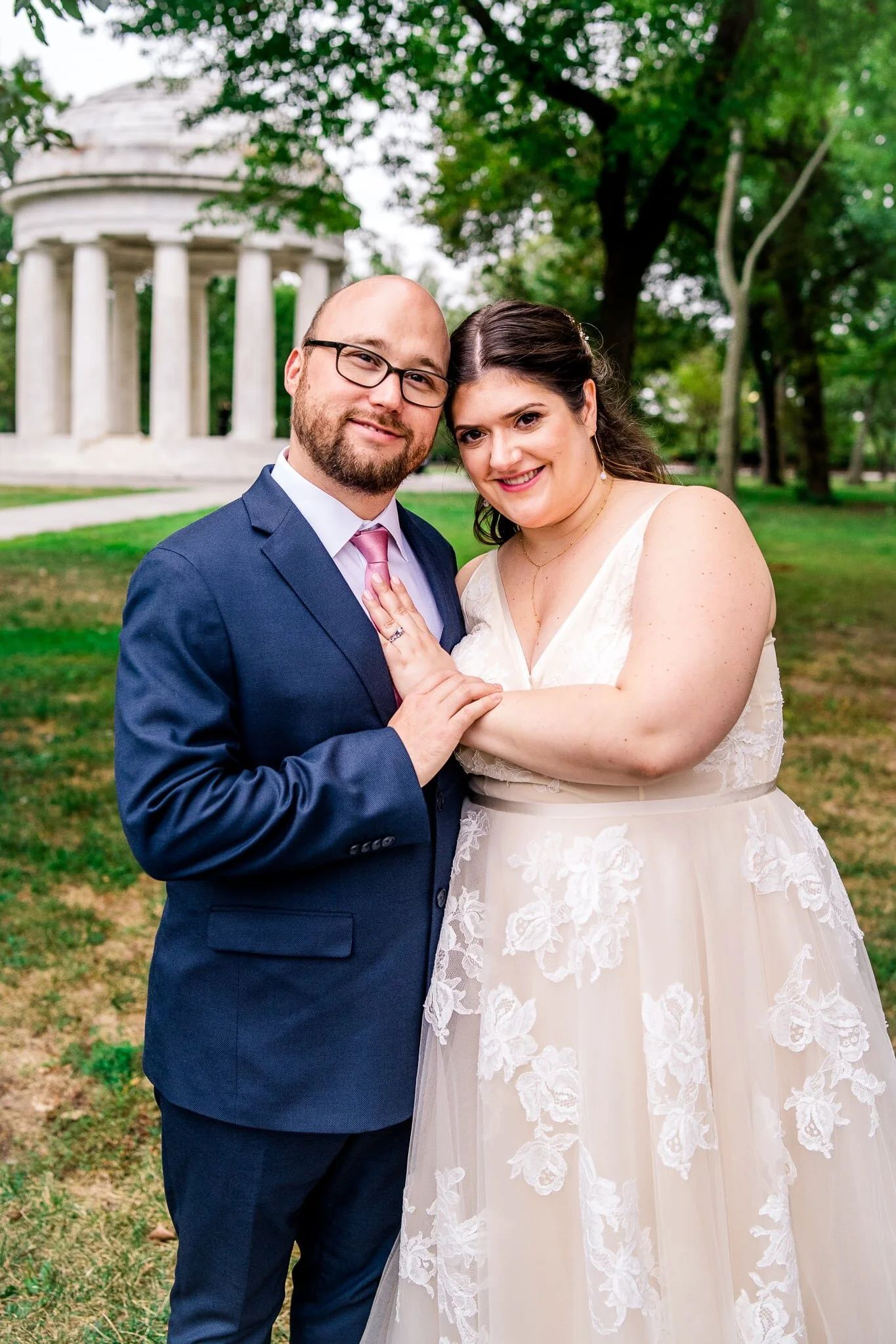 A bride and groom stand together with heads leaning toward each other on their fall wedding day in front of the DC War Memorial in Washington, DC