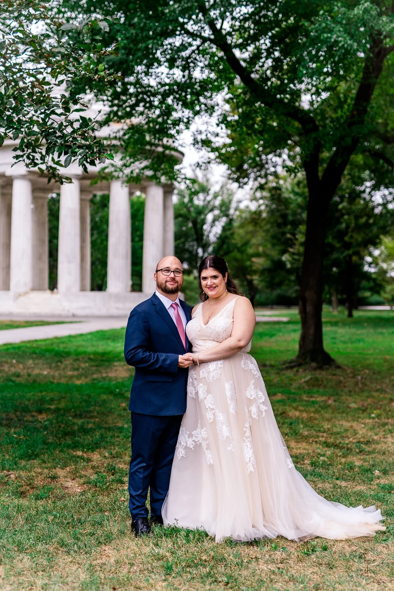 A bride and groom stand together holding hands on their fall wedding day in front of the DC War Memorial in Washington, DC