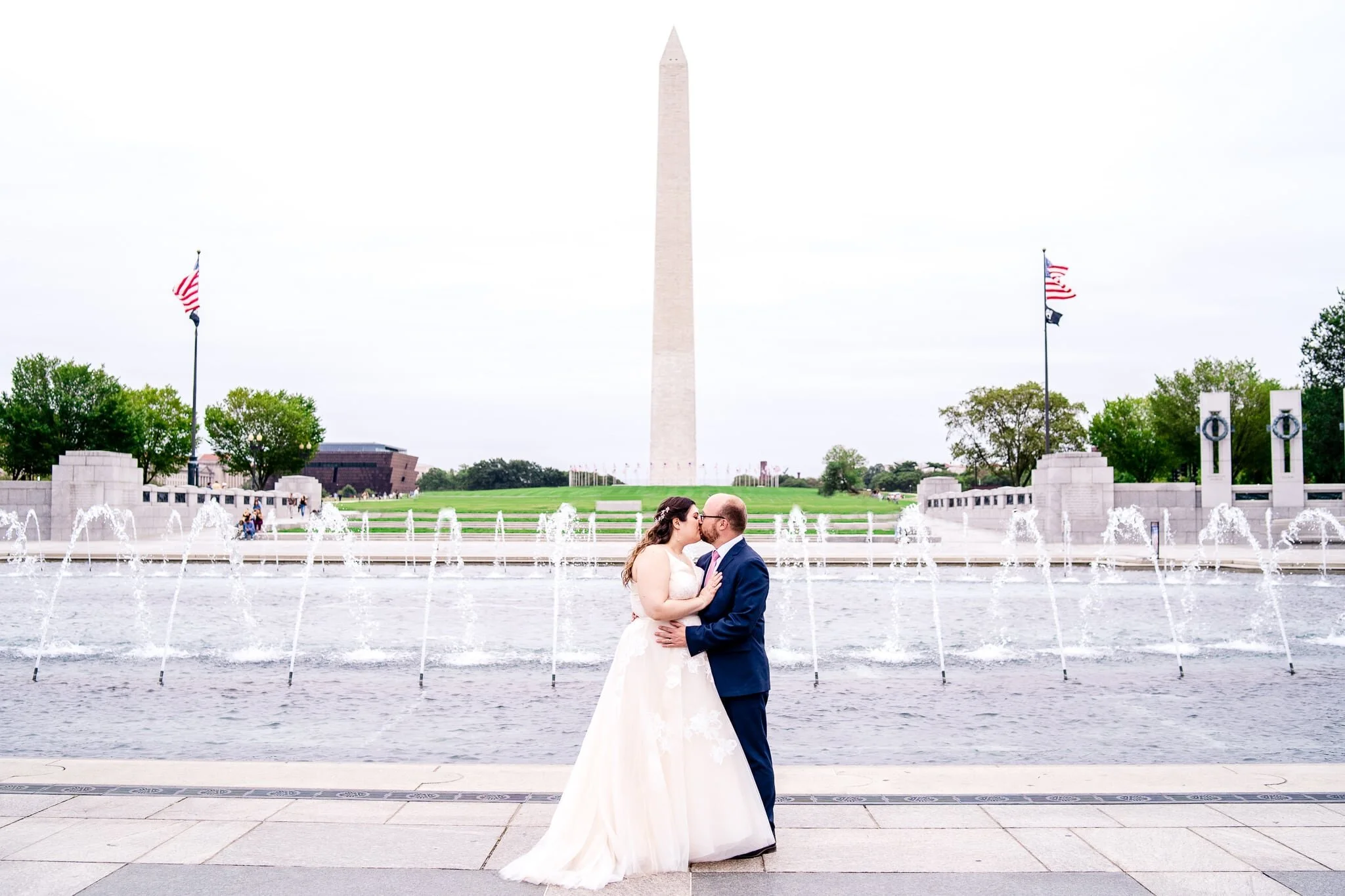A bride and groom share a romantic kiss on their fall wedding day at the WWII Memorial in front of the Washington Monument in Washington, DC