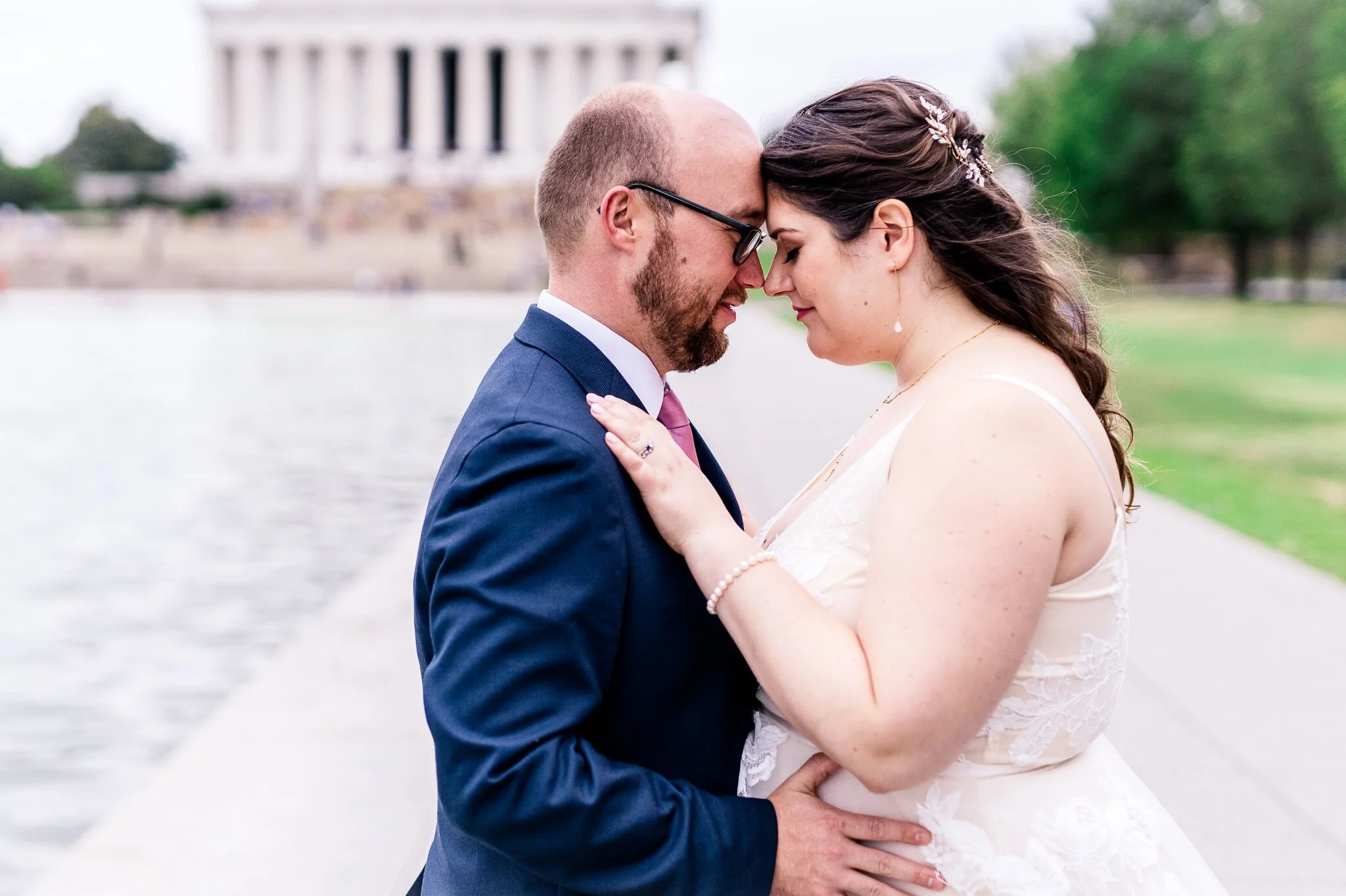 A bride and groom pose together with foreheads and noses together on their fall wedding day at the Reflecting Pool in front of the Lincoln Memorial in Washington, DC