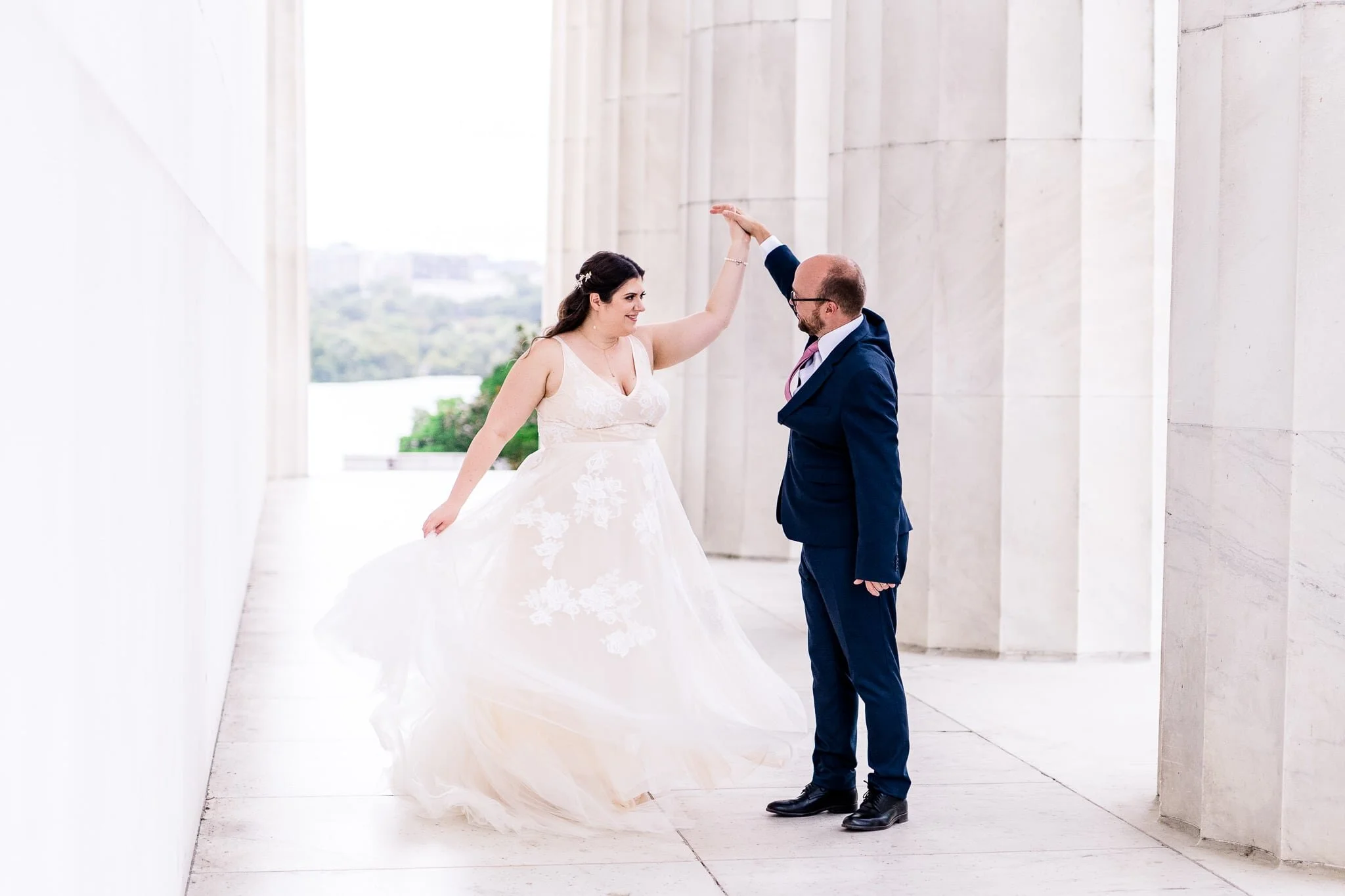 A bride and groom dance together and the groom twirls his bride as her tulle dress swirls around her on their wedding day at the Lincoln Memorial in Washington, DC