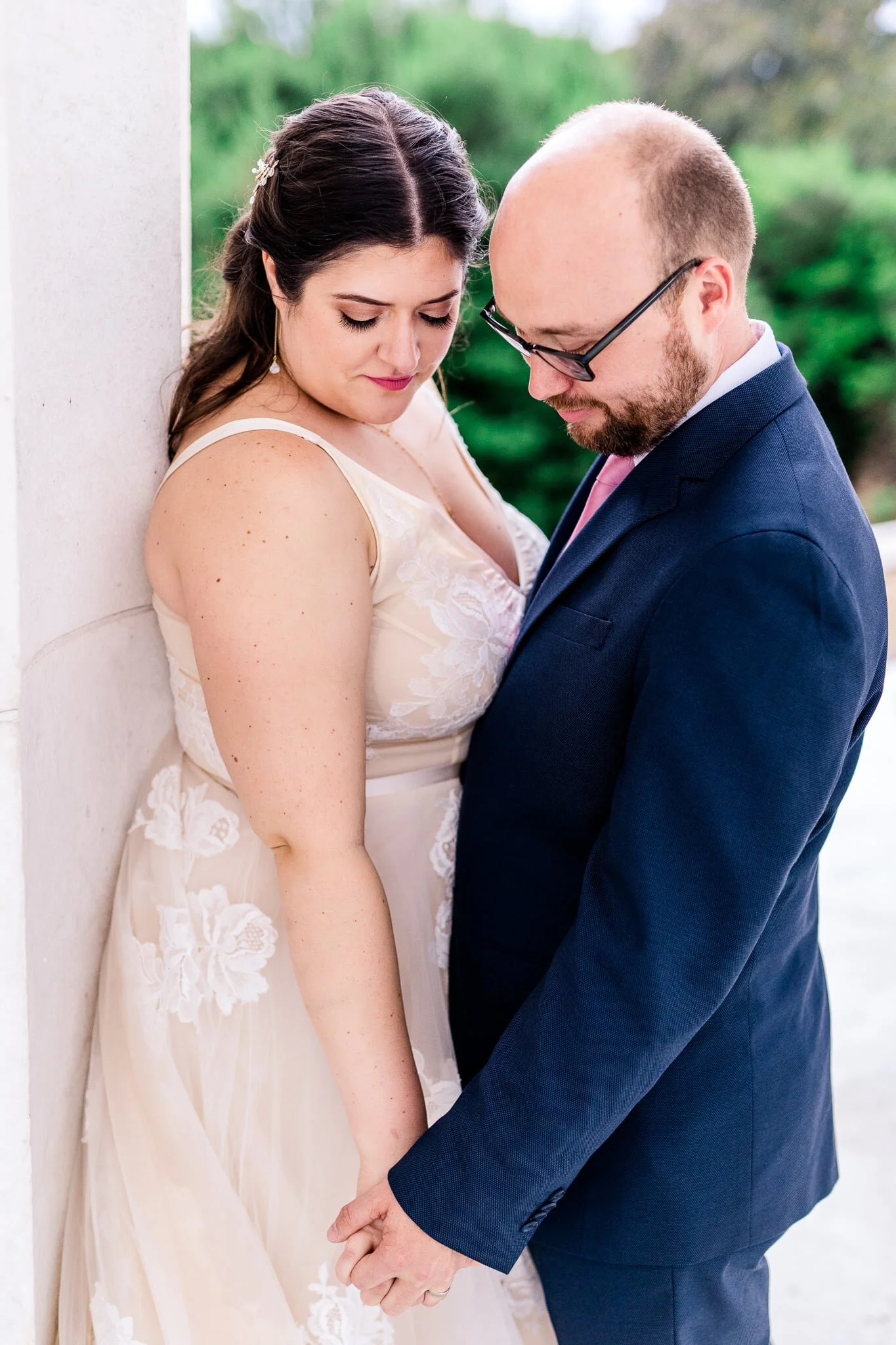 A bride and groom hold hands as they lean against a marble column on their wedding day at the Lincoln Memorial in Washington, DC