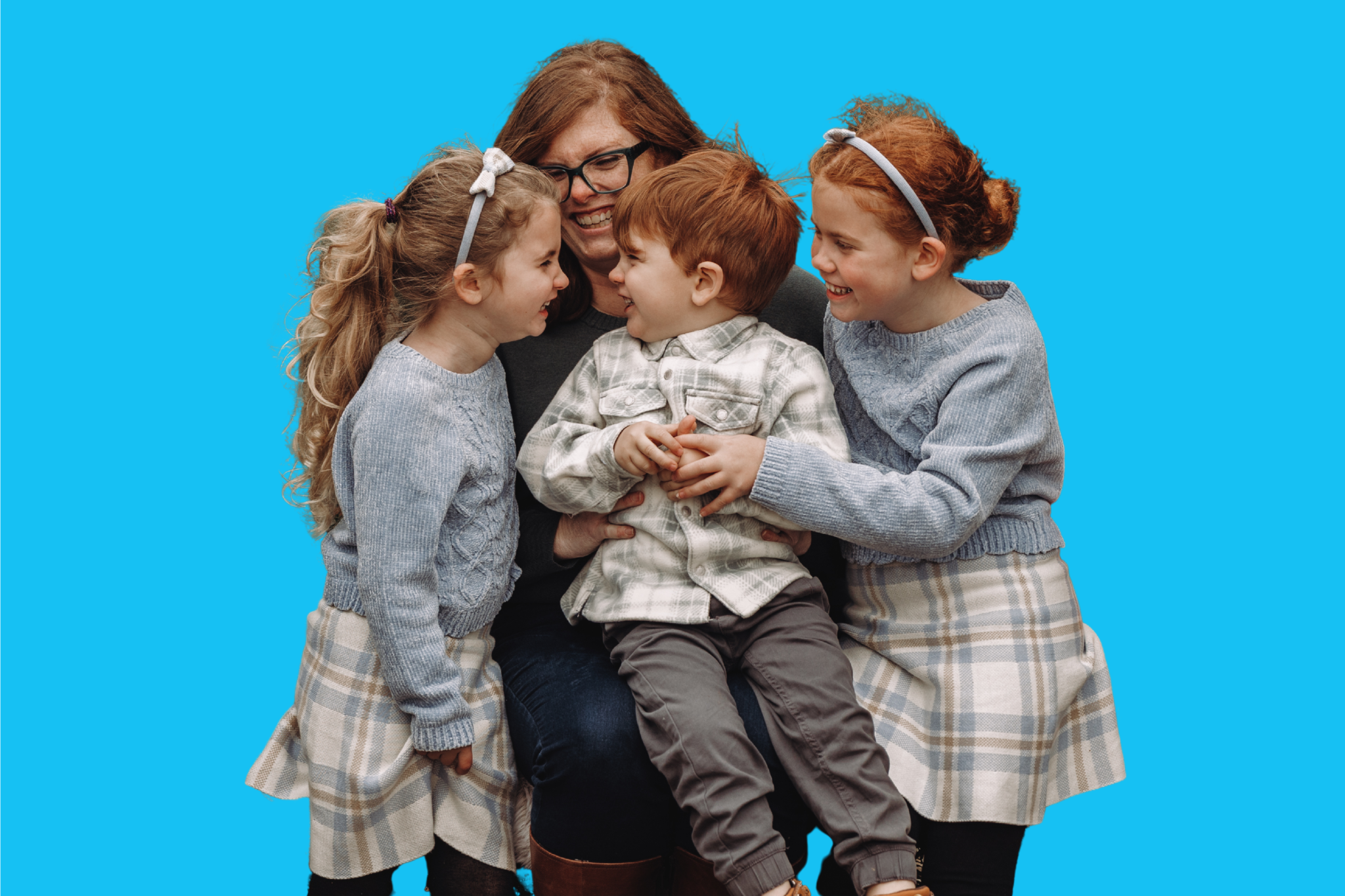 A picture of Allison, a glasses-wearing redhead, and her three children. The youngest, a redheaded boy (3) is sitting on her lap; the middle, a six-year old blonde, is smiling looking at him. The oldest, an 8 year old redhead, is on the other side.