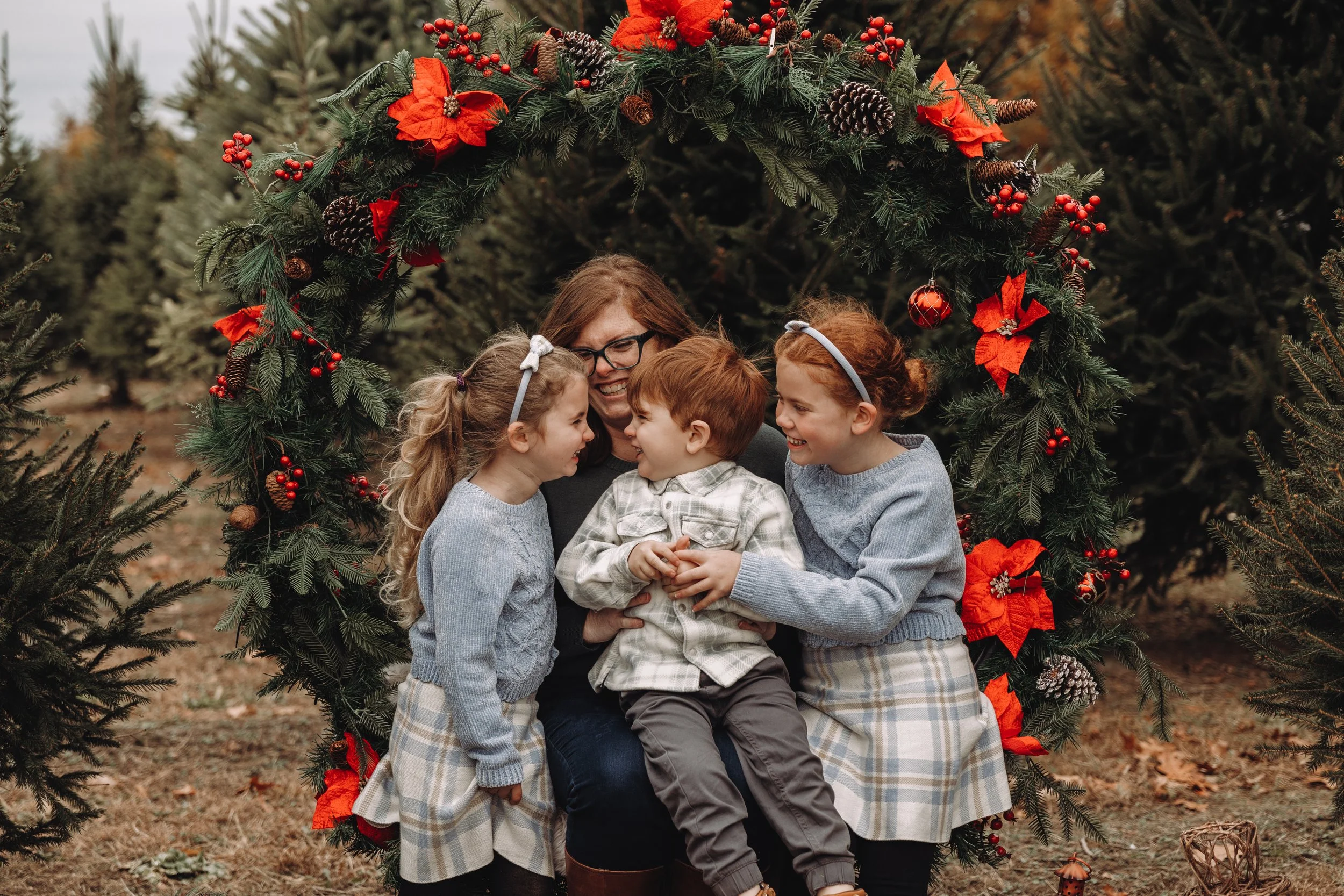 A picture of Allison, a glasses-wearing redhead, and her three children. The youngest, a redheaded boy (3) is sitting on her lap; the middle, a six-year old blonde, is smiling looking at him. The oldest, an 8 year old redhead, is on the other side.