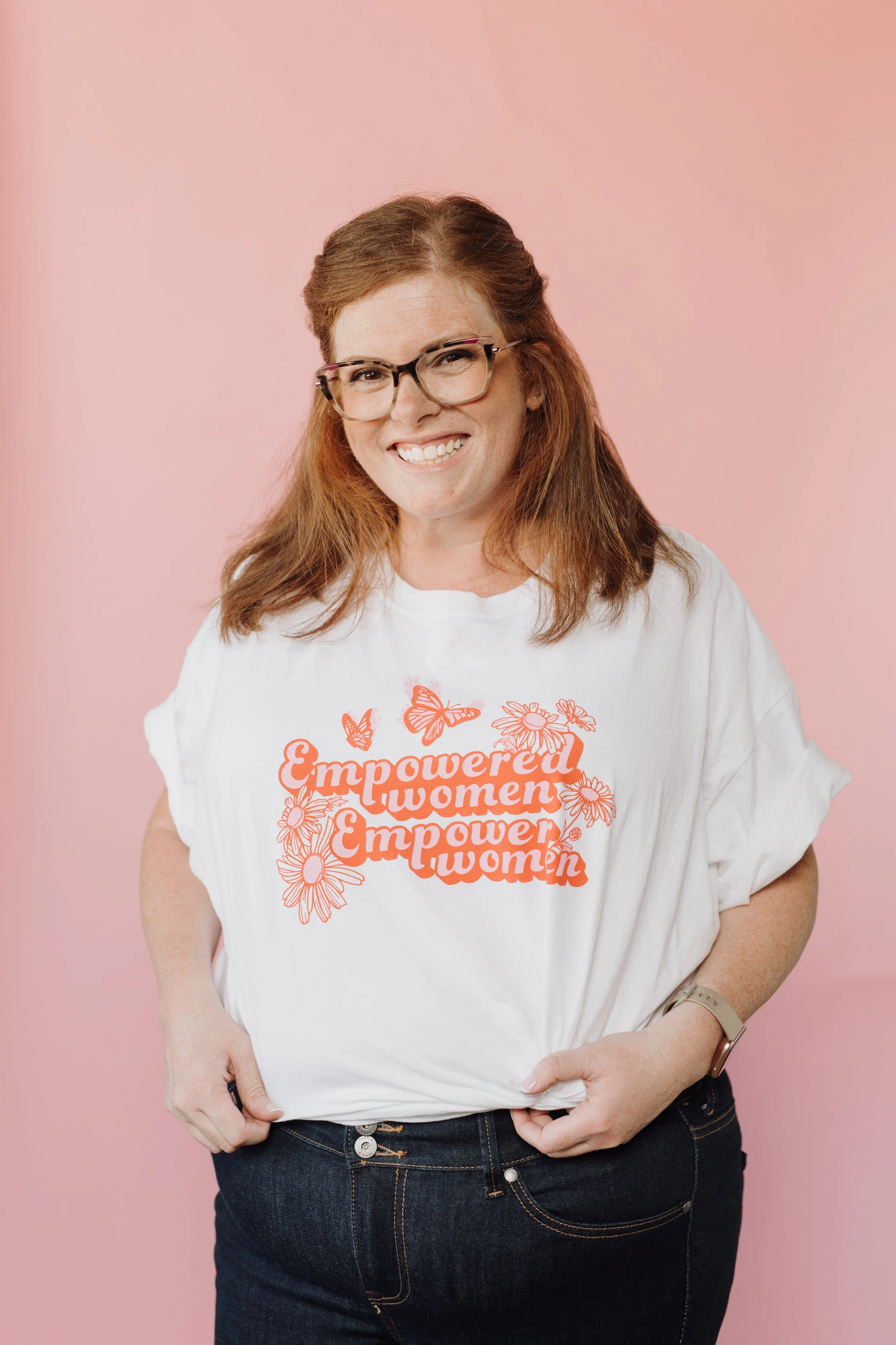 Allison, a glasses-wearing redhead in a white shirt with pink lettering that says "Empowered women empower women" against a pink backdrop.