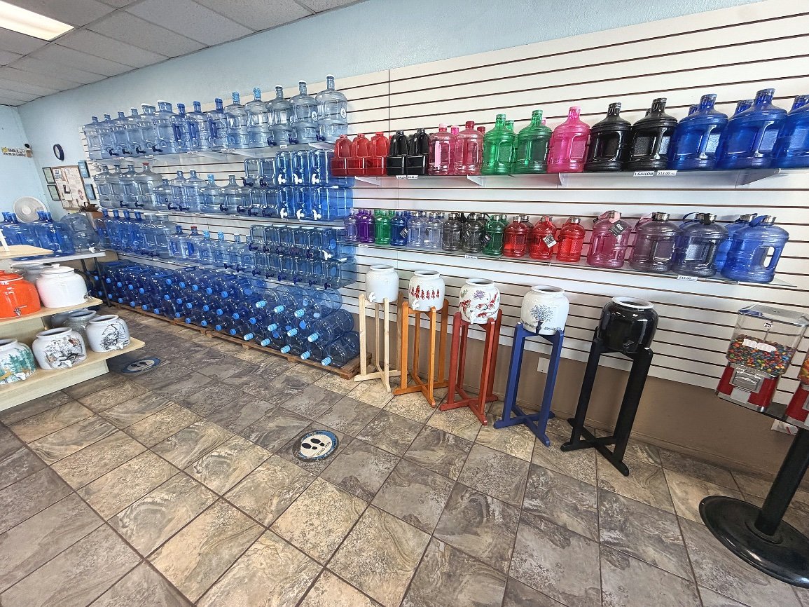 Wall of water bottles and jugs with colorful caps at Fresh Alka Water in San Diego — bottle caps, seals, and reusable jugs for purified and alkaline water refills