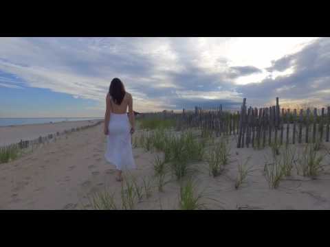 Young brunette woman walking along tunes in white dress