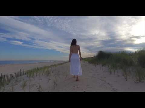 Young brunette woman in white dress walking along sand dunes