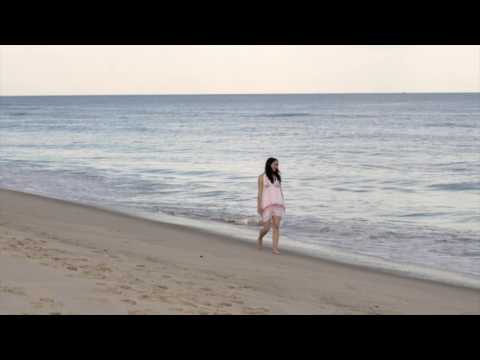 Young brunette in short white dress walking down sandy beach