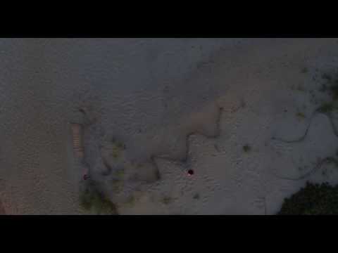 Aerial descent on sandy beach upon young bruntte woman