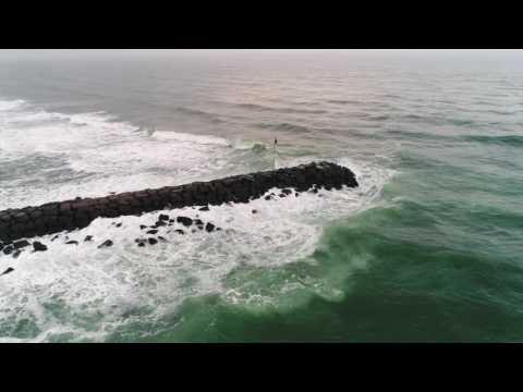 Aerial pan around tip of jetty in sormy winter ocean waters