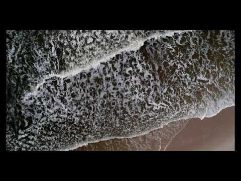Aerial rotational view above dark ocean waves crashing on beach