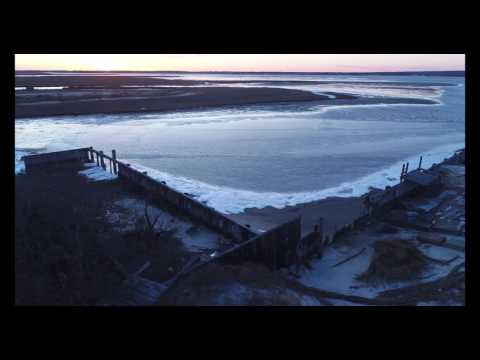 Slow pan shot of frozen bay and old wooden bulkhead at sunset
