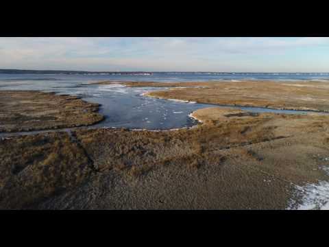 Low aerial pass over snowy beach road and out across frozen bay