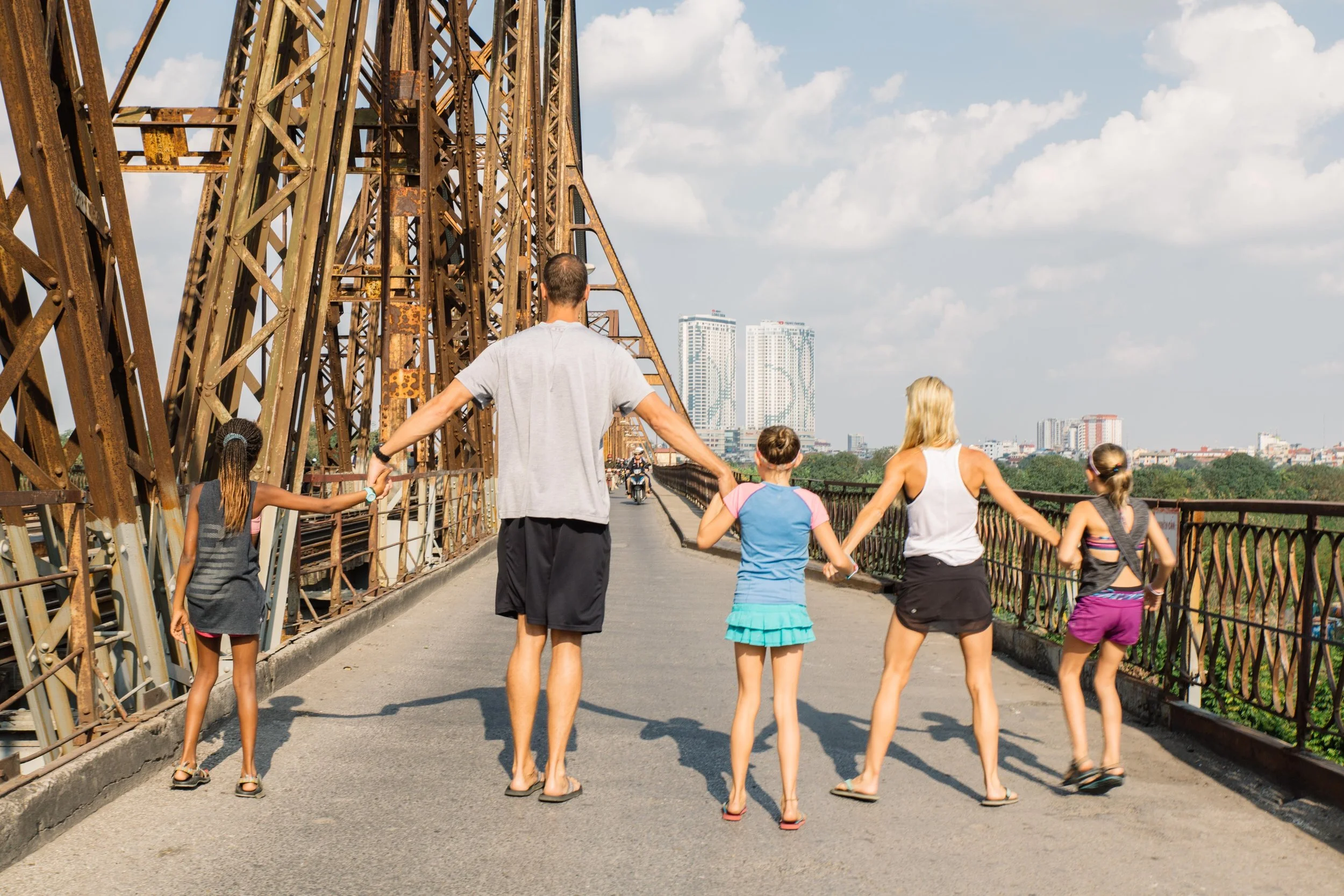 Traffic paused just long enough for a quick family photo on the historic Long Bien Bridge in Hanoi, Vietnam. The bridge which spans over 1 mile and is one of the longest in Asia, crosses the Red River and connect Hanoi to the Northern provinces of Vietnam. It was bombarded heavily and often by the USA during the Vietnam War, but always re-built and still stands strong today. It is now only used for scooters and pedestrians access. 