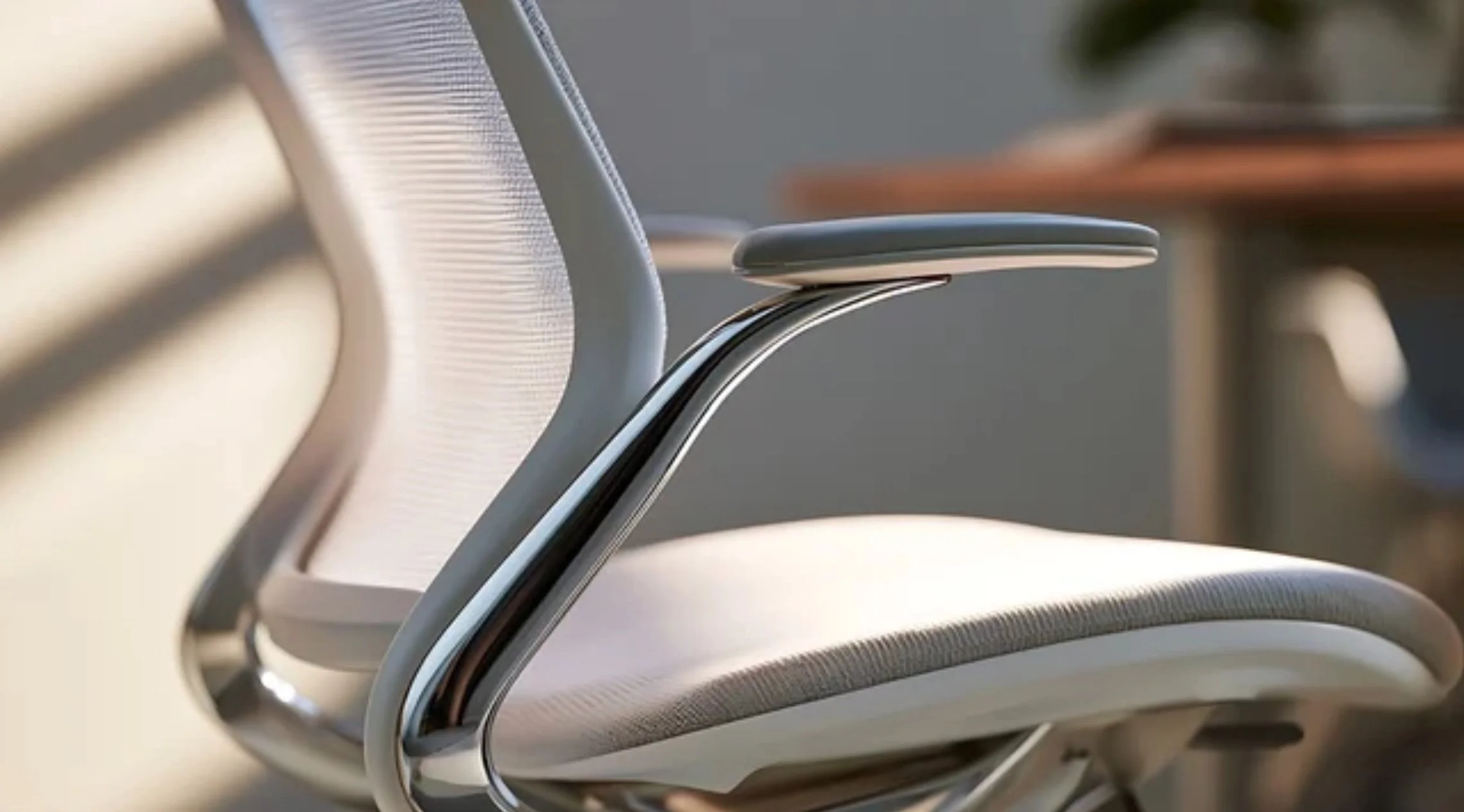 Close-up of a modern ergonomic executive office chair featuring a breathable mesh backrest, contoured upholstered seat, adjustable armrests, and polished metal detailing.