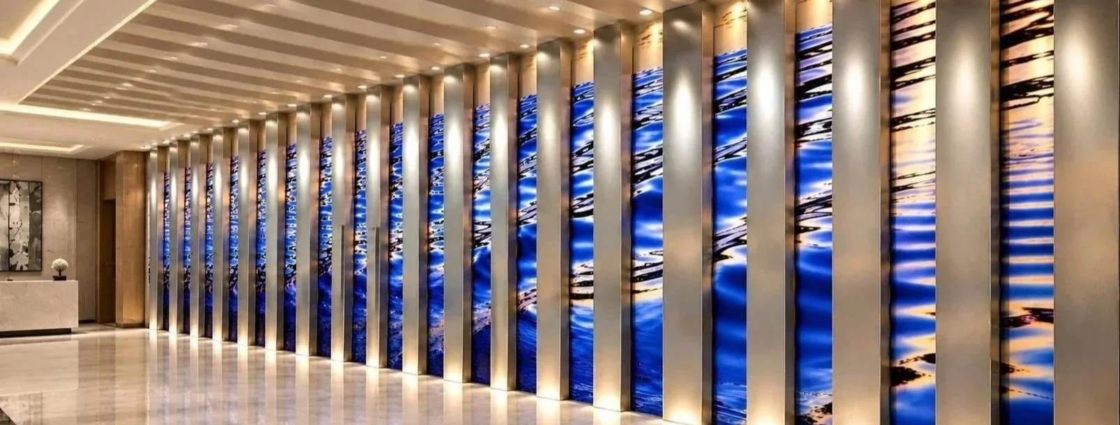 Custom architectural wall installation designed by Silver Chase Design, featuring vivid blue photographic imagery printed on reflective aluminum panels with projecting metal beams creating sculptural depth and dimension.