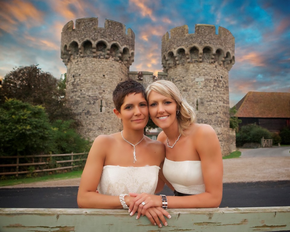 two brides leaning on the gate by the turrets