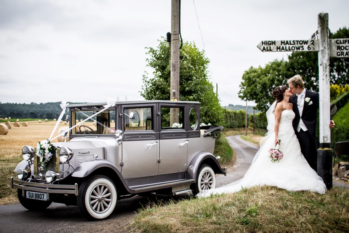 Bride and groom kissing with a car in the background