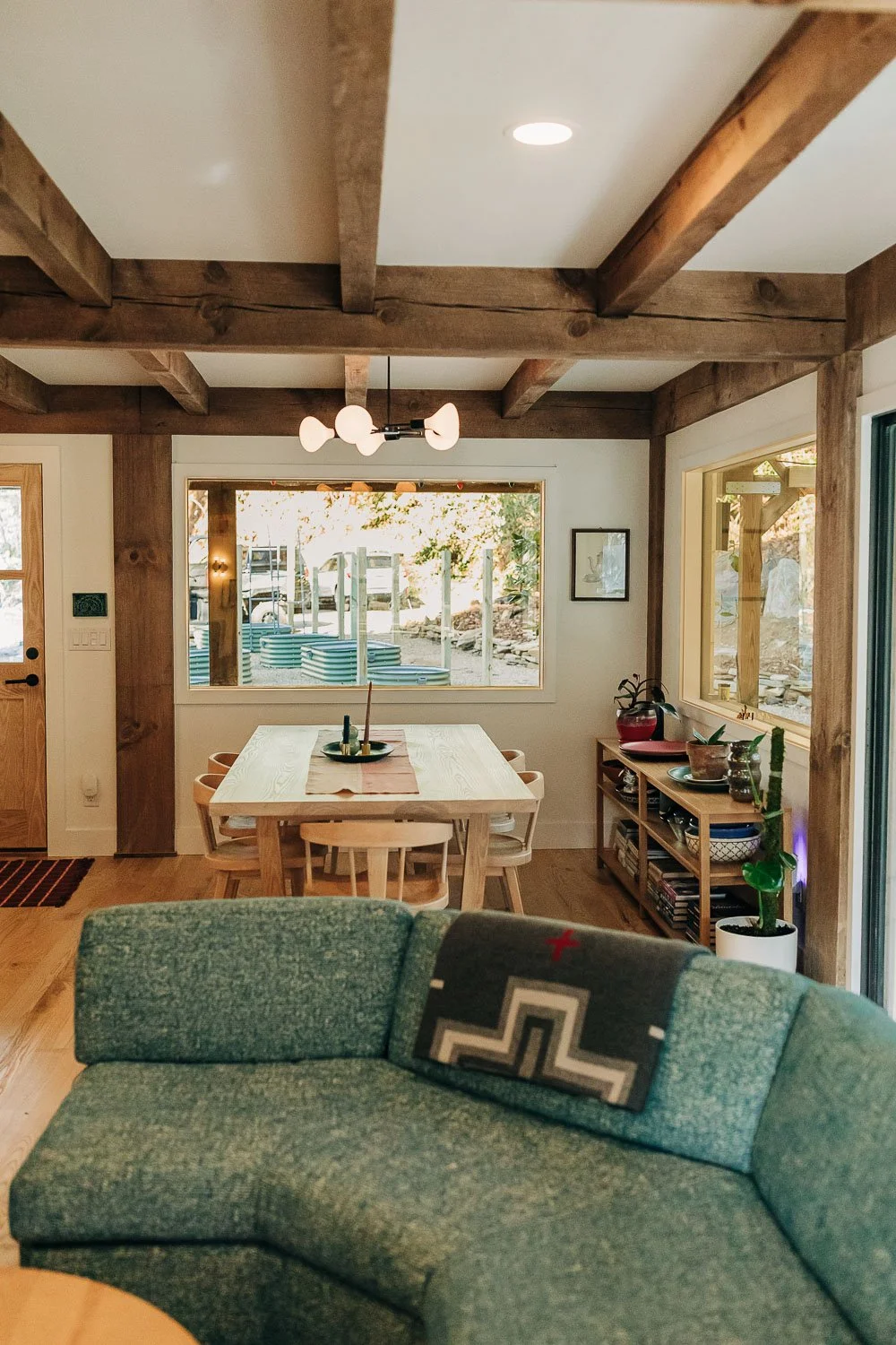 Living space with exposed wood beams, and open layout with teal mid century couch, white oak modern custom table and chairs made in North Carolina