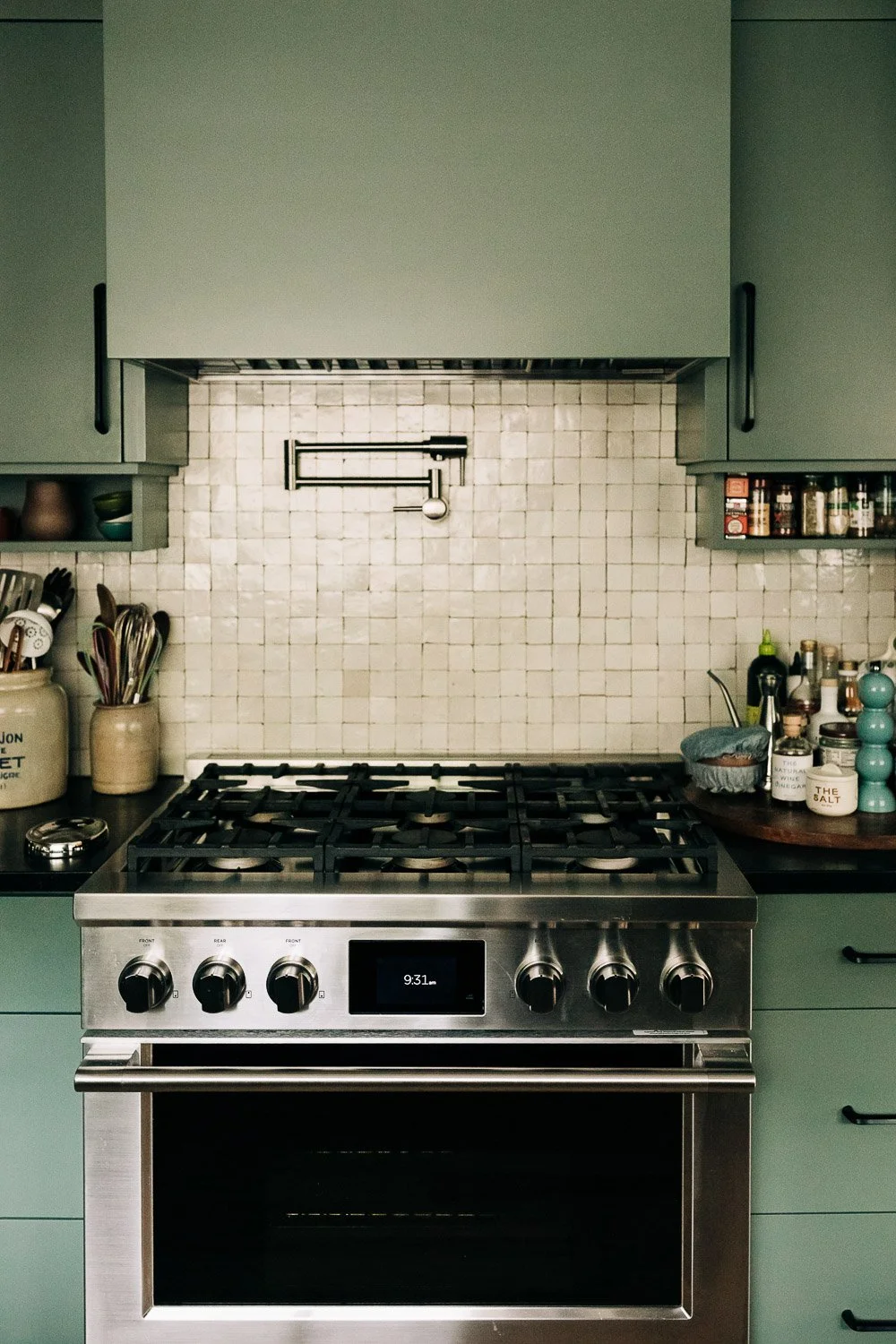 Gas range with integrated pot filler, tile backsplash, and painted cabinetry with custom millwork storage in Bat Cave NC kitchen