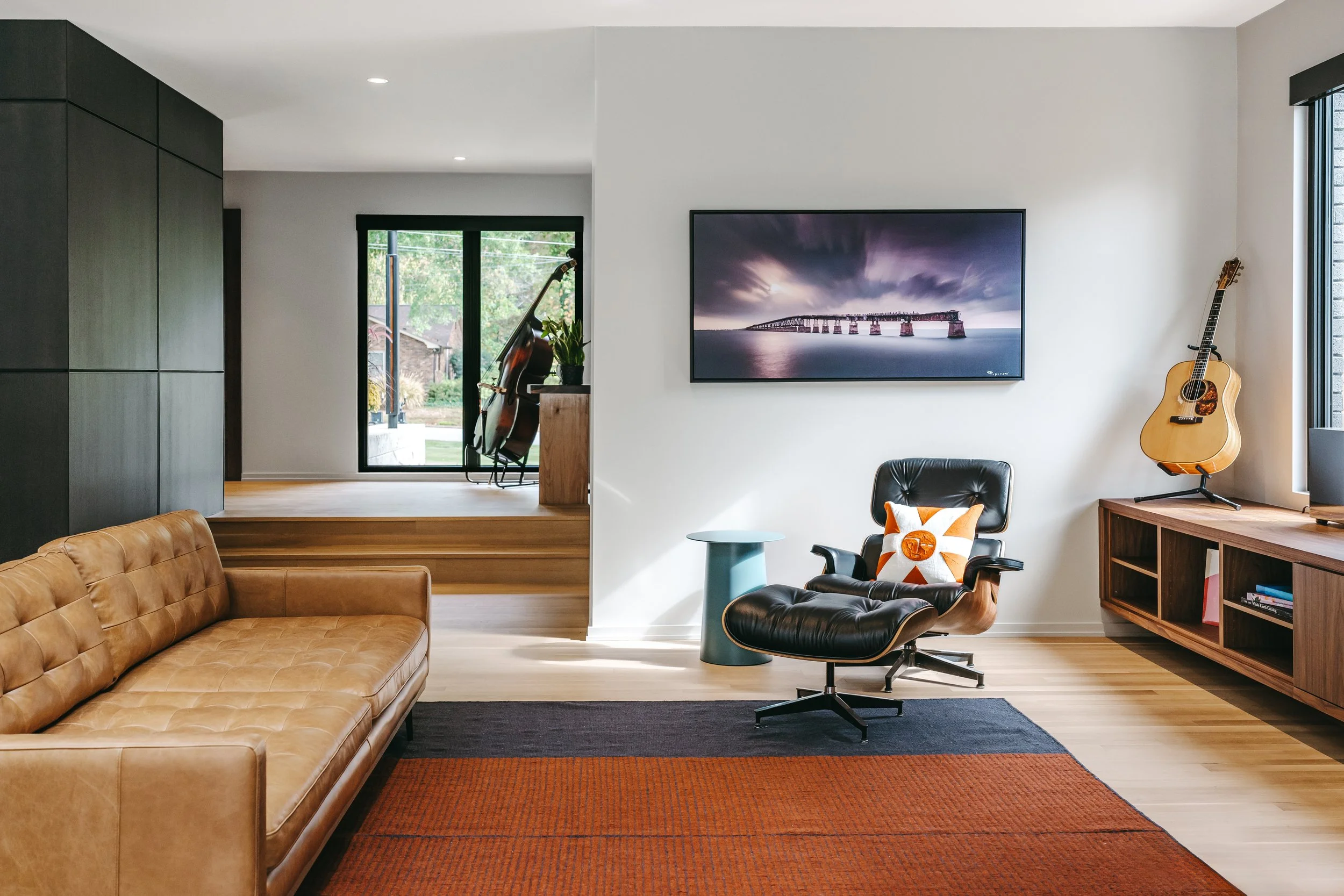 Guitar, modern leather couch, with an Eames black leather chair, Custom woodwork by Sunnyside Millwork Custom 20-foot floating black walnut entertainment center with grain-matched veneer drawer fronts, under lighting, precision scribed to fit irregul