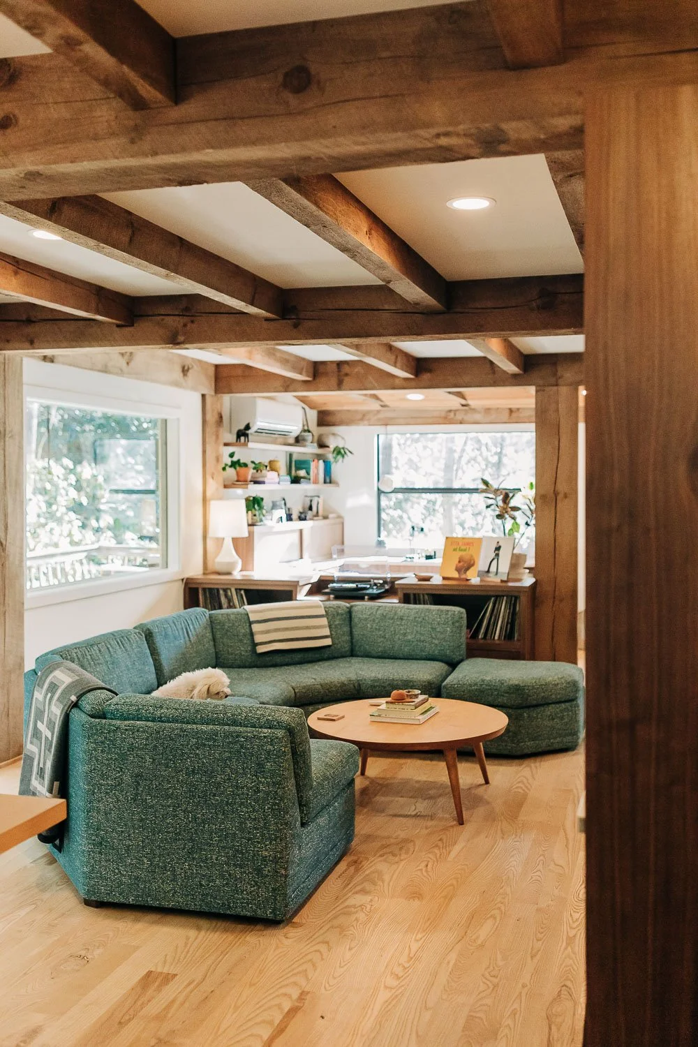 Living space with exposed wood beams, and open layout with teal mid century couch, black walnut cabinetry made in North Carolina