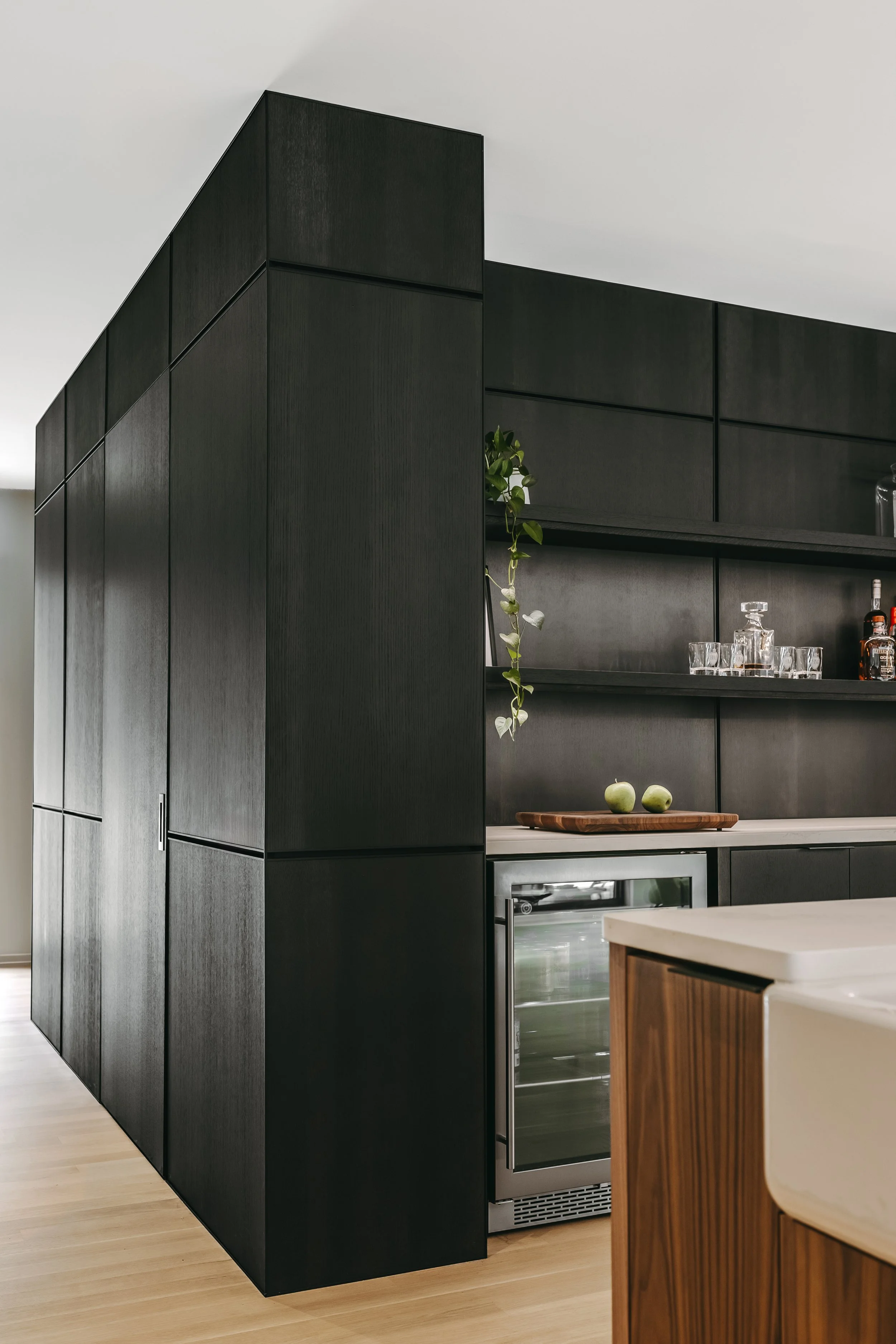 Custom woodwork by Sunnyside Millwork Black rift white oak panel wall with India ink finish and Fry Reglet aluminum reveals creating clean architectural wall transitions in modern kitchen bar remodel in Kernersville, North Carolina