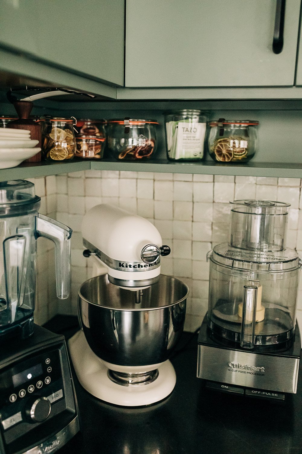 1 inch square white fire clay Italian Tile backsplash with custom painted green kitchen cabinetry, and small appliances on counter top like kitchen aid and food processor and various spices in North Carolina mountain kitchen remodel