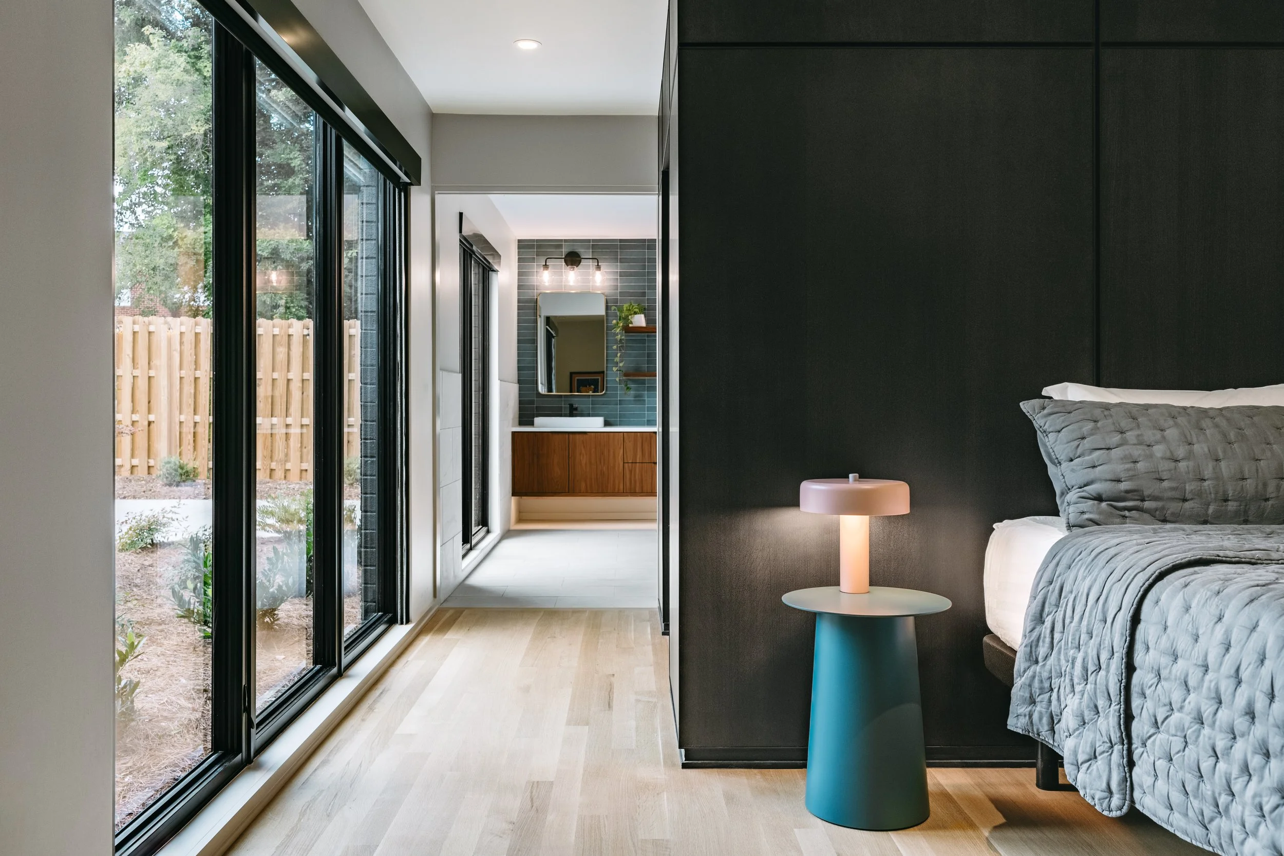 Custom woodwork by Sunnyside Millwork Black rift white oak panel wall with India ink finish and integrated flush seams behind bed, Floating walnut vanity with integrated lighting, quartz countertop, and custom millwork storage in modern bathroom desi