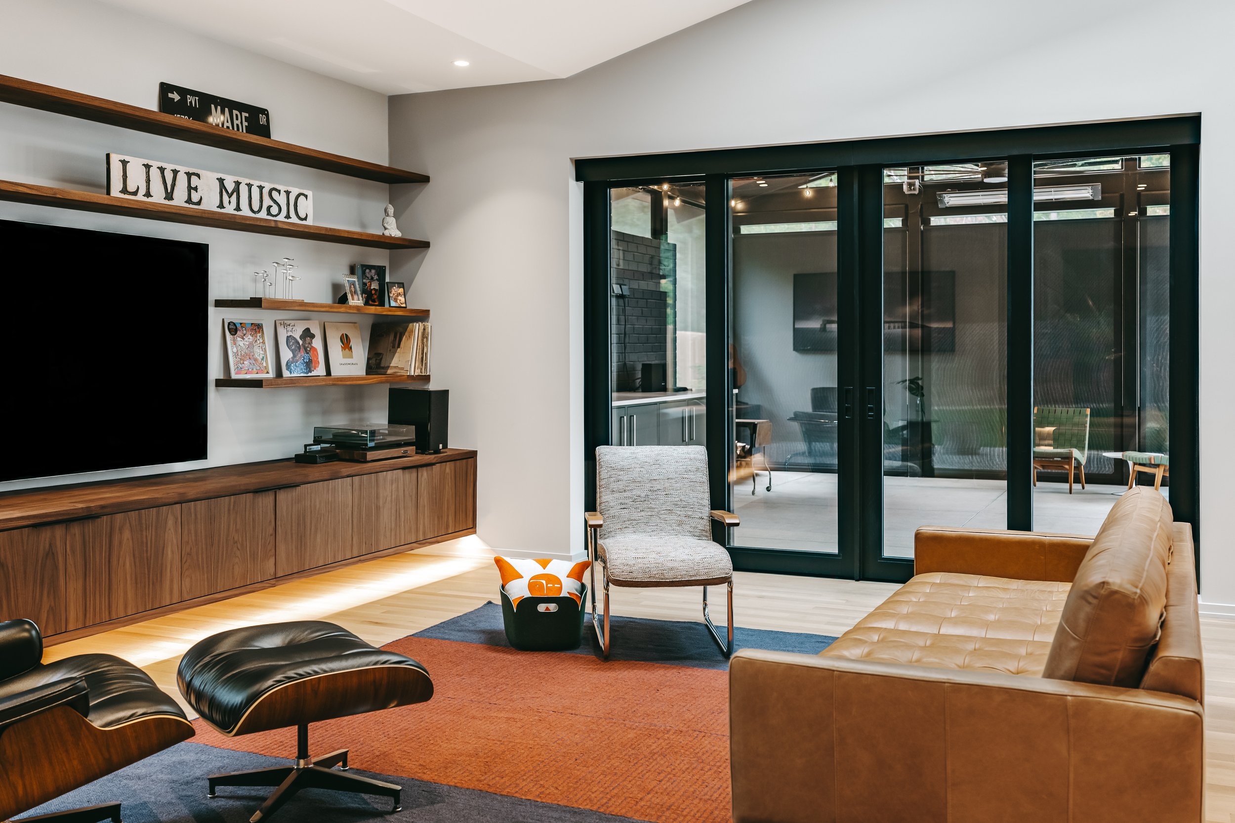 Modern living room with leather sofa, Eames lounge chair, and guitar, featuring a custom 20-foot floating black walnut media center with grain-matched cabinetry, integrated storage, and under lighting by Sunnyside Millwork