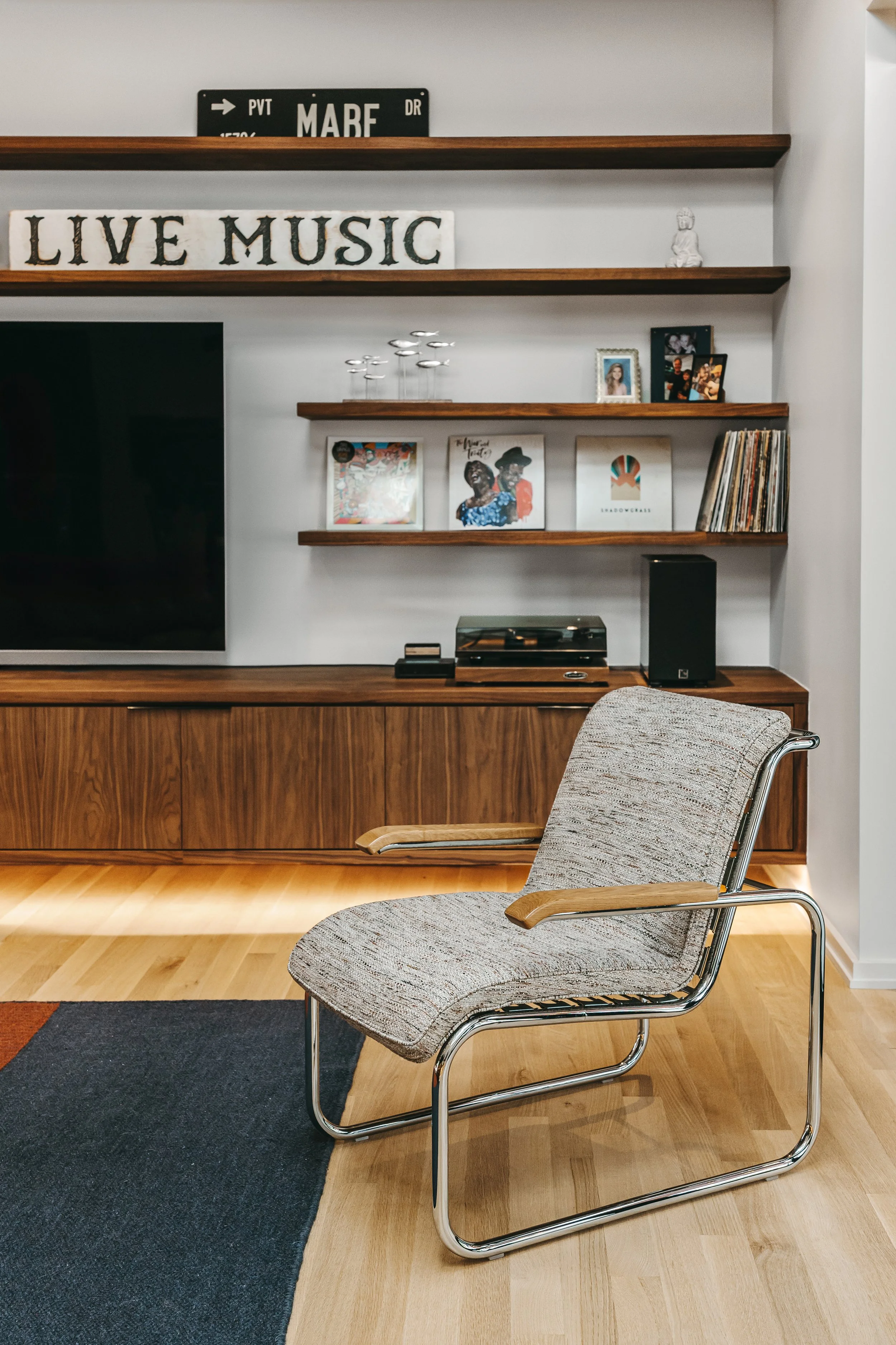 Modern living room with leather sofa, Eames lounge chair, and guitar, featuring a custom 20-foot floating black walnut media center with grain-matched cabinetry, integrated storage, and under lighting by Sunnyside Millwork