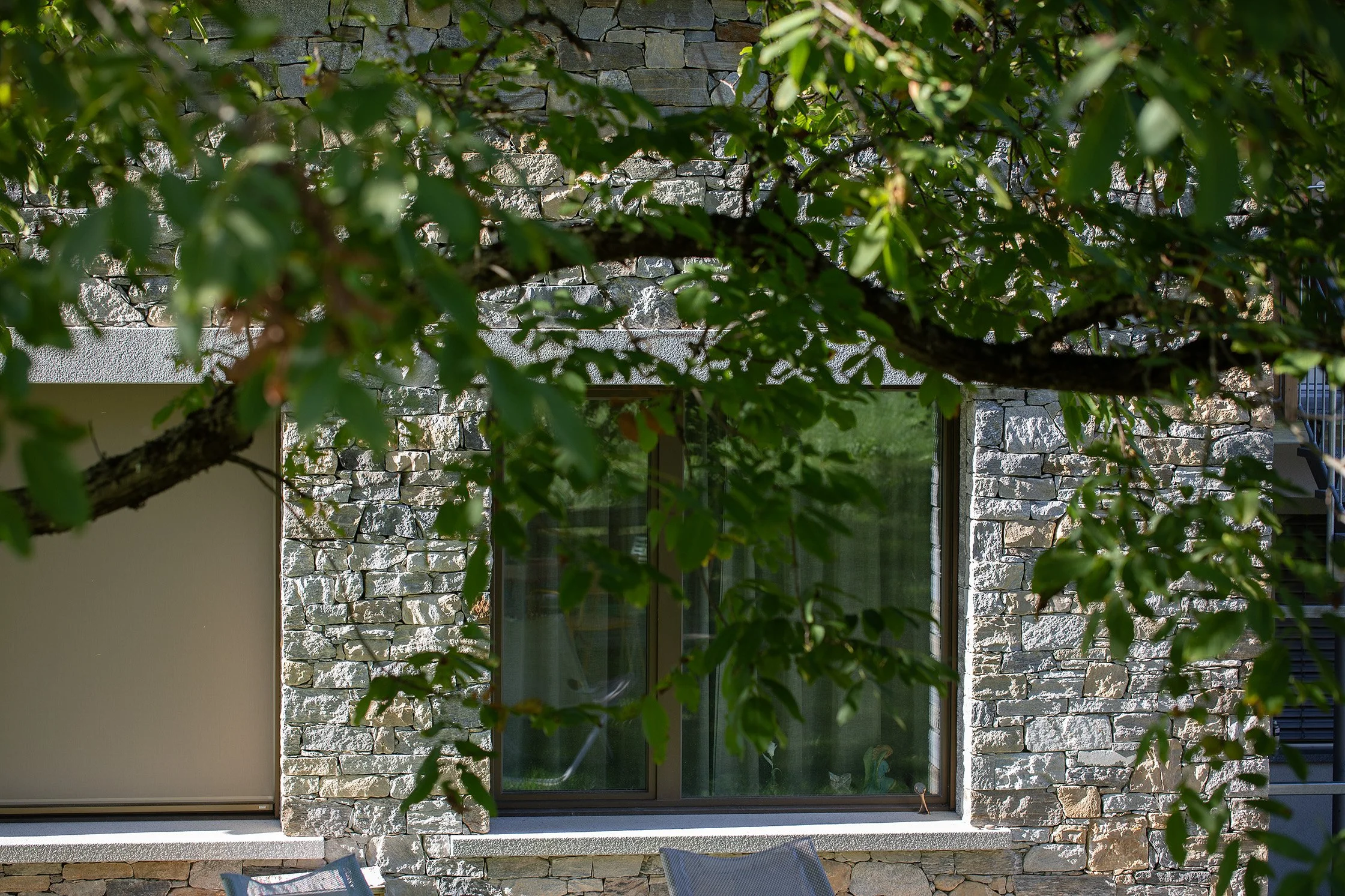 Mehrgenerationenwohnen C - Fenster in der Natursteinfassade hinter Baumzweigen.jpg