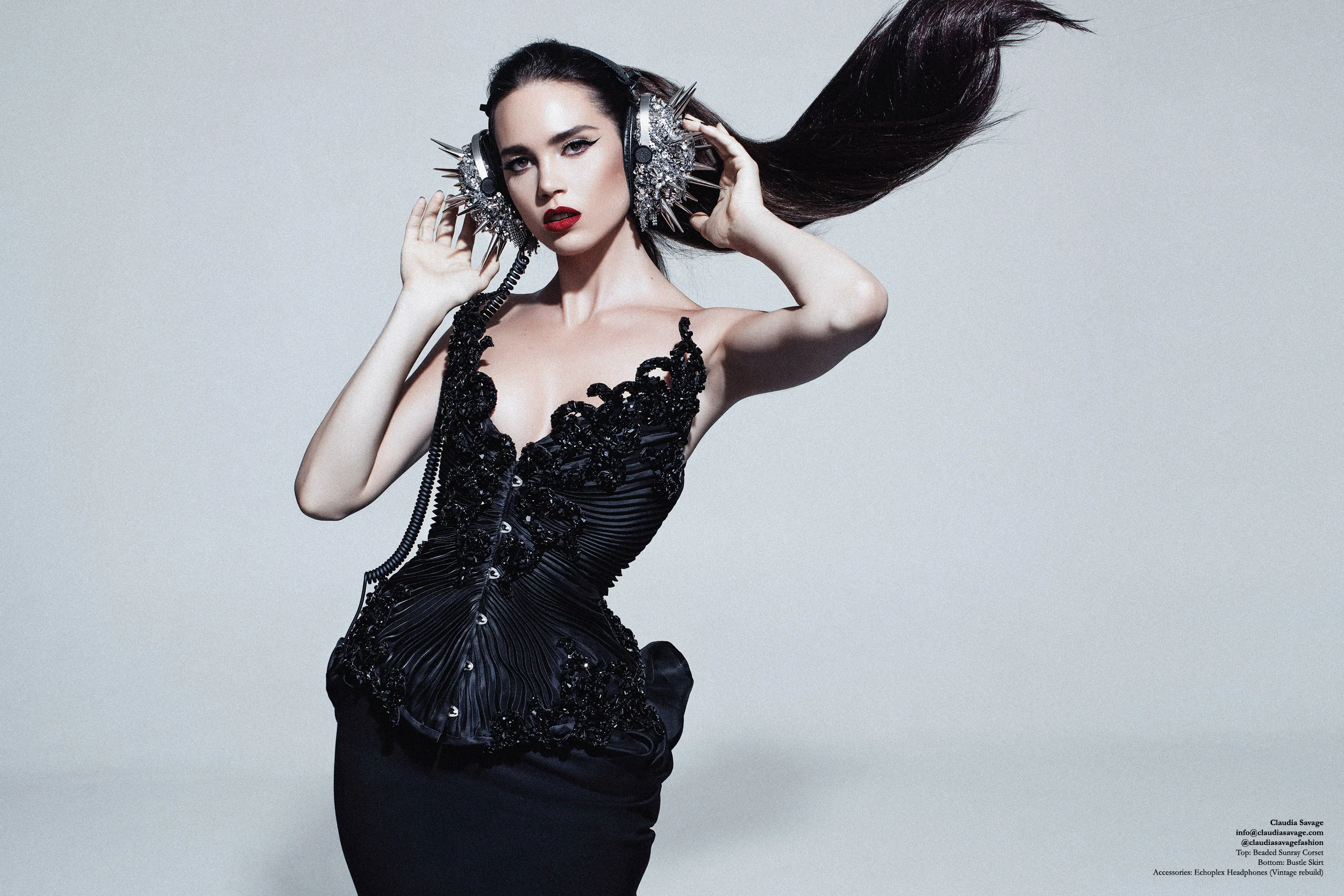 Model wears a made to measure corset with black silk organza pleating, encrusted with sculptural lace which has been coated in hand stitched jet Swarovski Elements over a black under-bust wool pencil skirt with a sculpted silk organza bustle. The silver “Echoplex” headphones are coated in silver coloured studs and spikes, draped in metallic mesh and hand encrusted with silver Swarovski Elements.