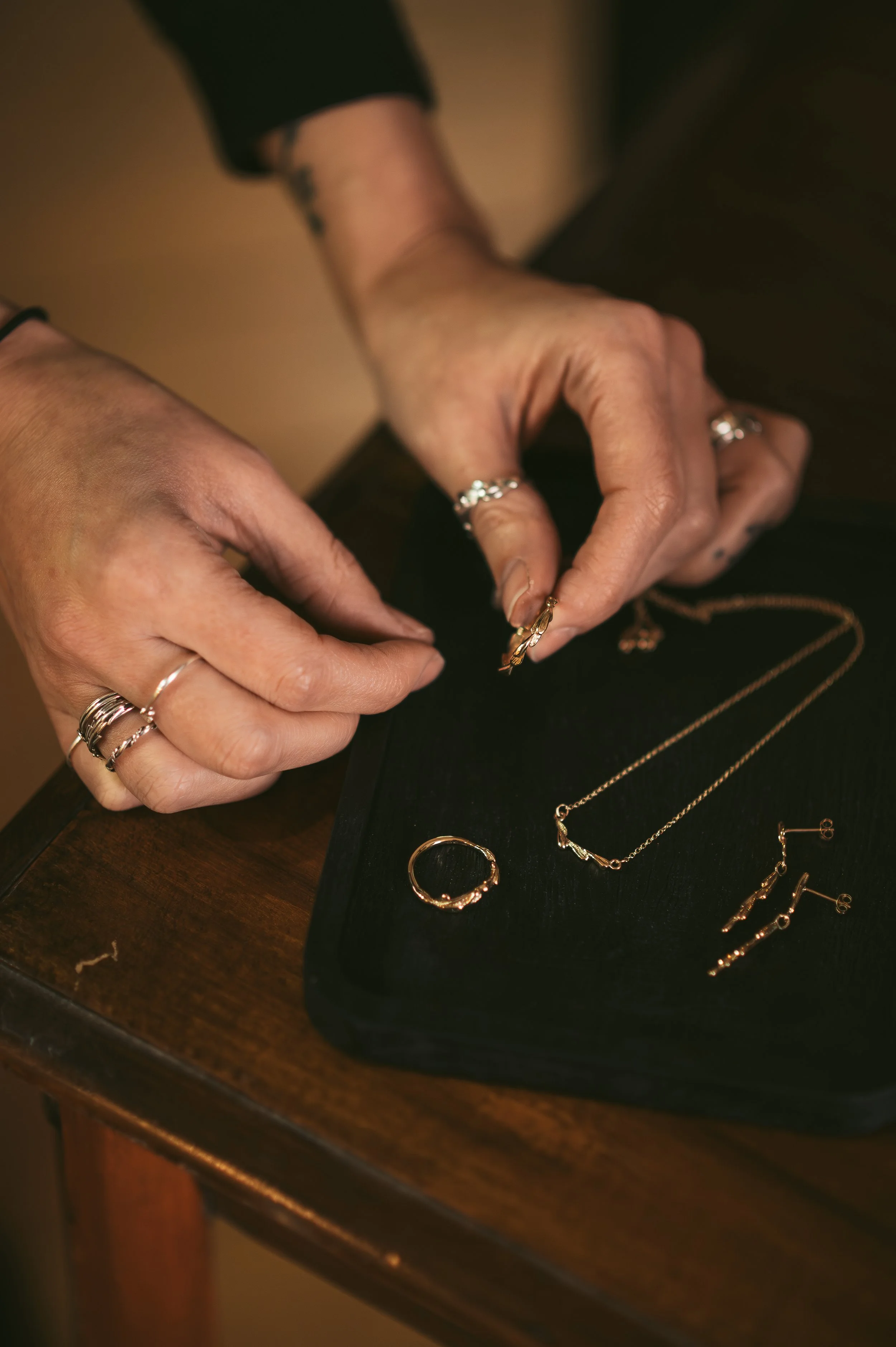 A close up of Scottish jewellery designer Holly McAfee's hands, picking up a ring from a selection of jewellery on a black tray.