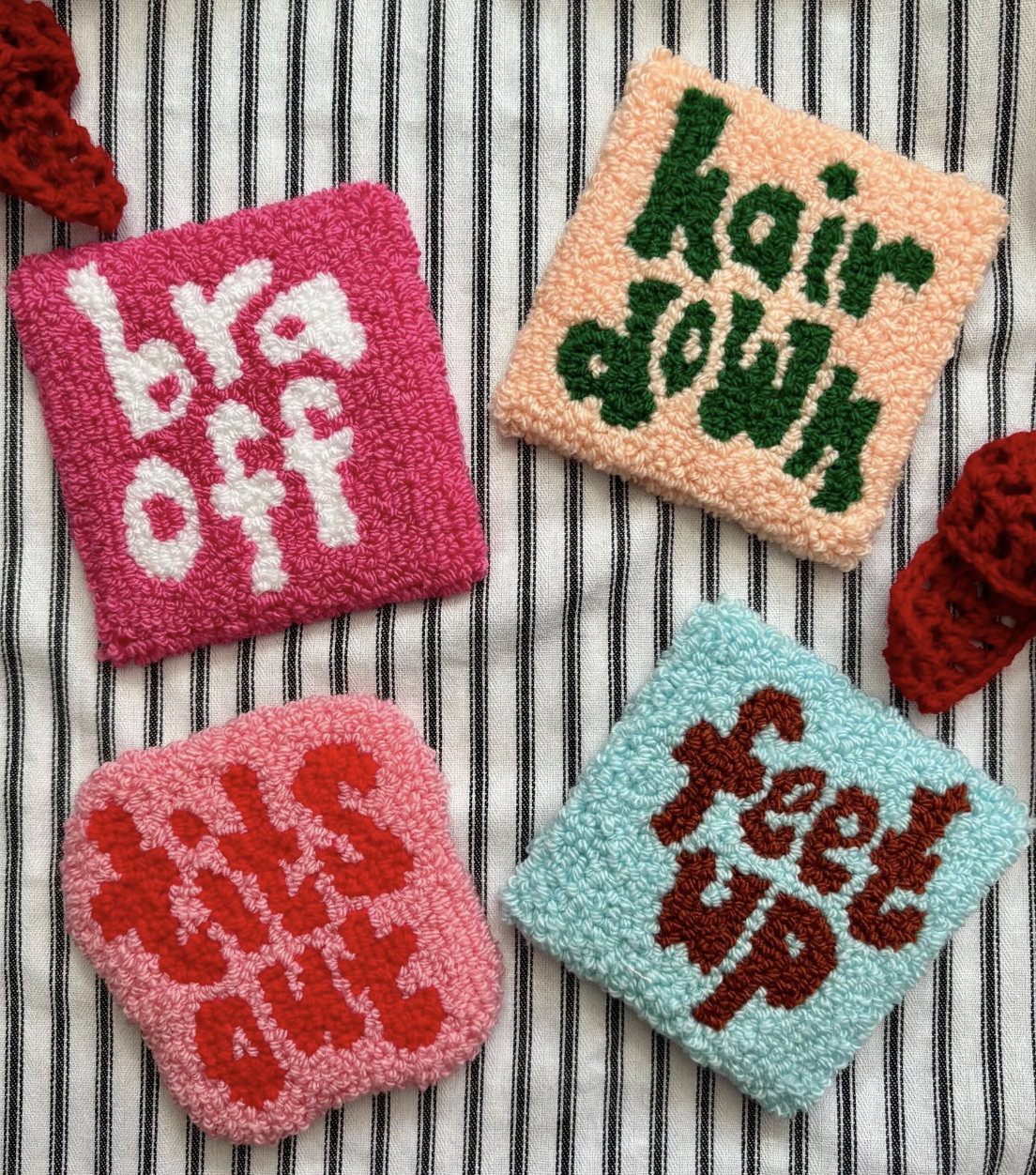 Four punch needle coasters sit on a striped fabric background. One reads "hair down", one reads "feet up"