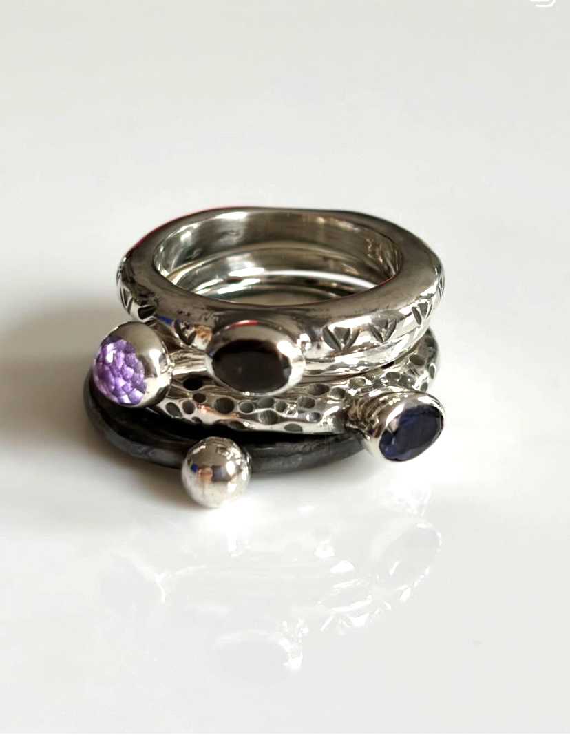 A stack of four hammered silver rings, each featuring a different gemstone, each totally unique
