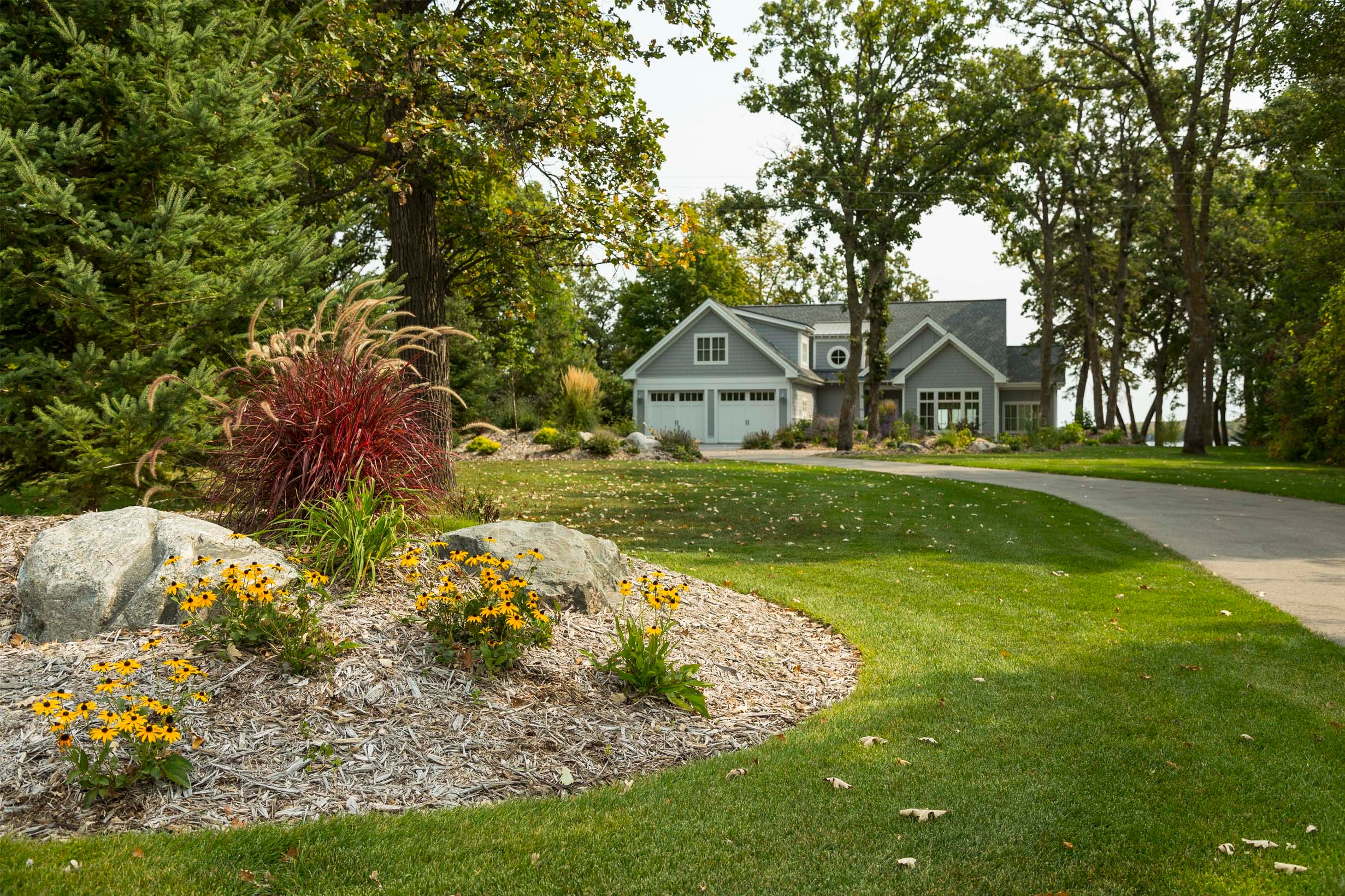 Berming, natural stone outdroppings, and a variety of colorful perennial plantings create a unique entry sequence for this beautiful home on Pelican Lake.