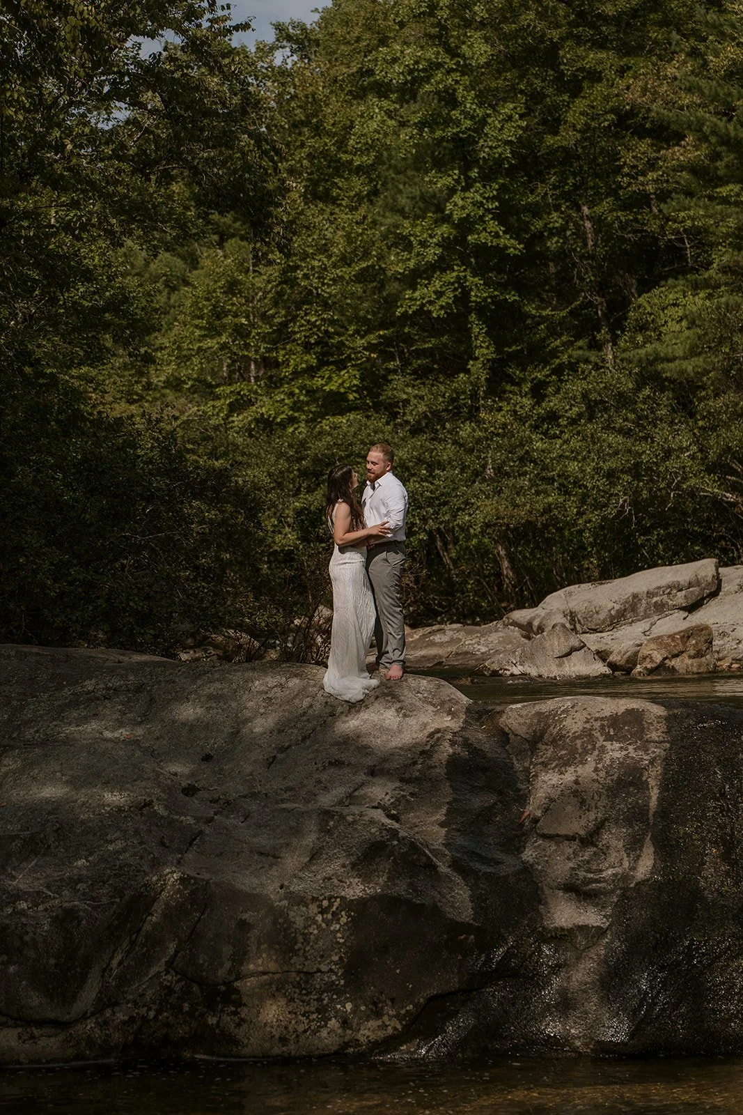 An eloping couple embrace atop a moody waterfall