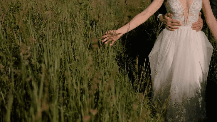 A bride brushes her hand through mountain grass