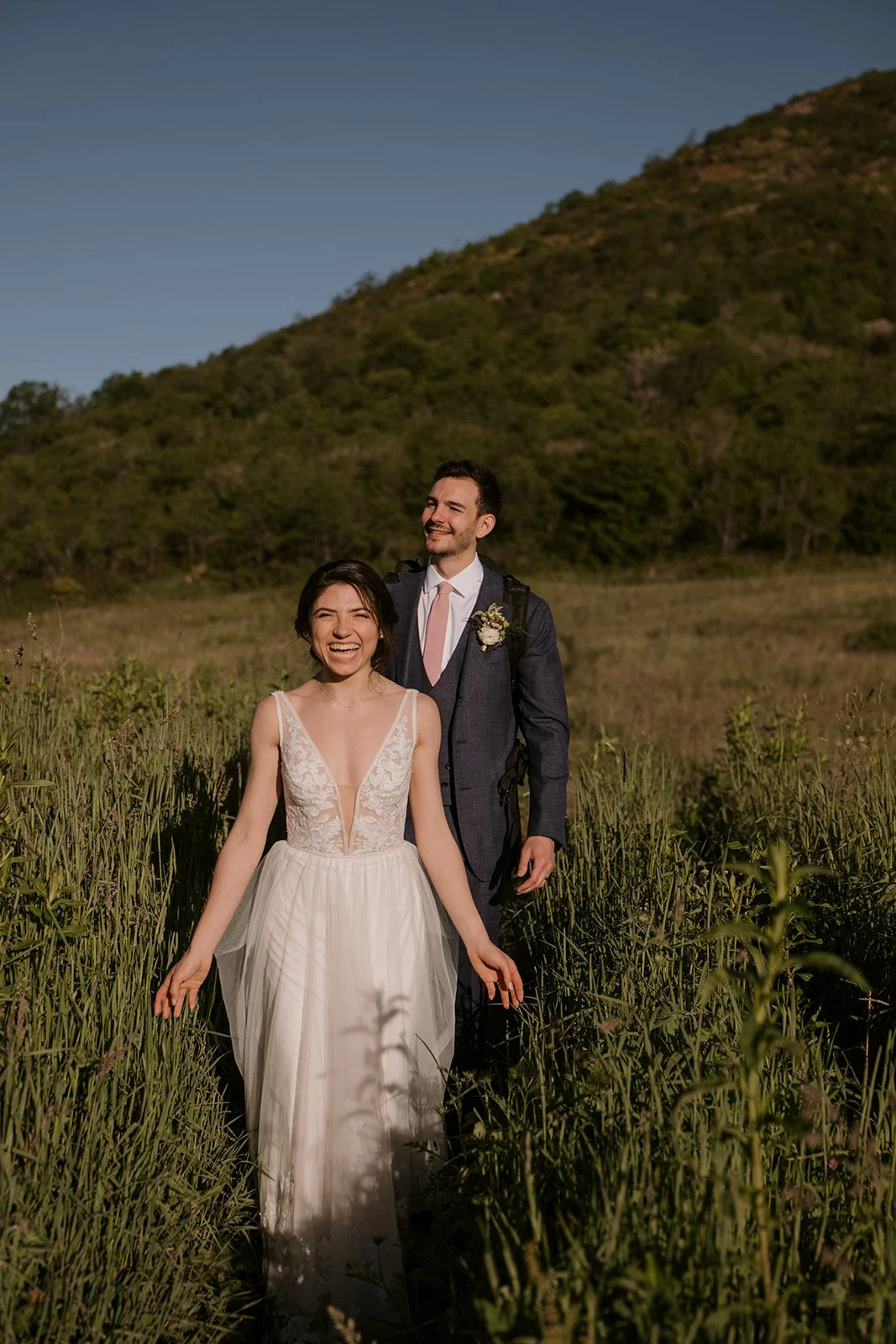 An ecstatic bride and groom take in a mountain prairie in wedding attire