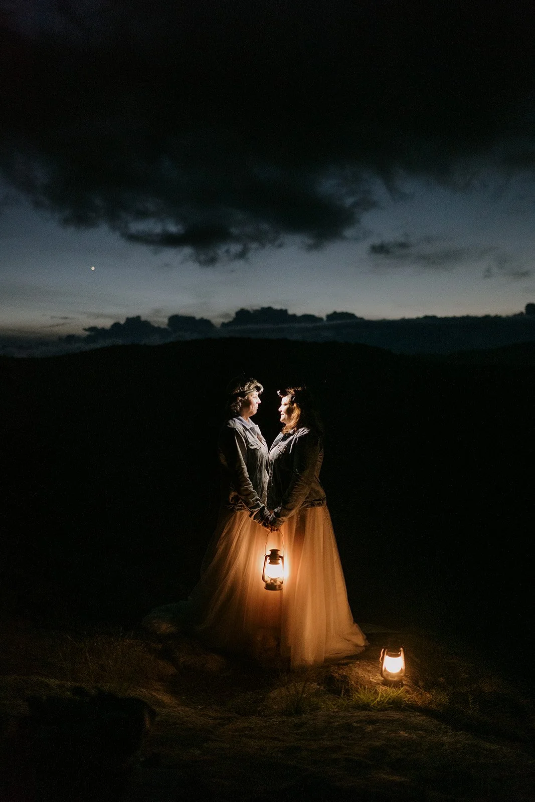 Two brides pose for an artful nighttime shot in the mountains