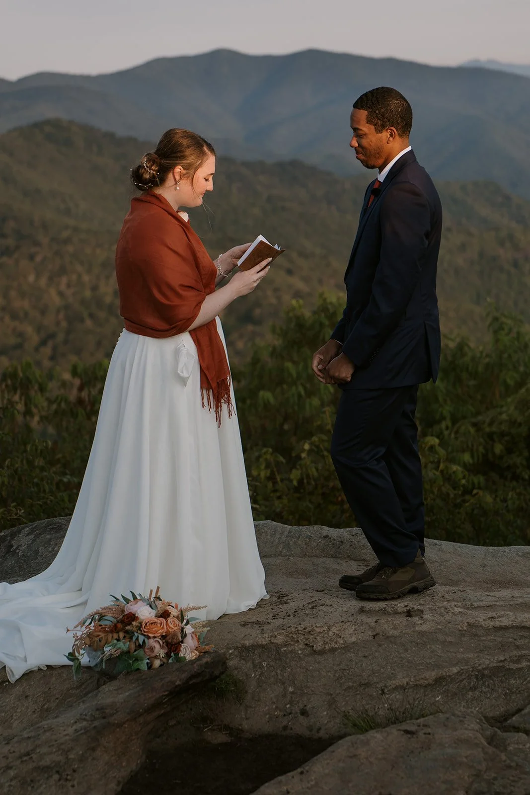 A bride recites her vows to her groom atop a mountainside bathed in sunset warmth
